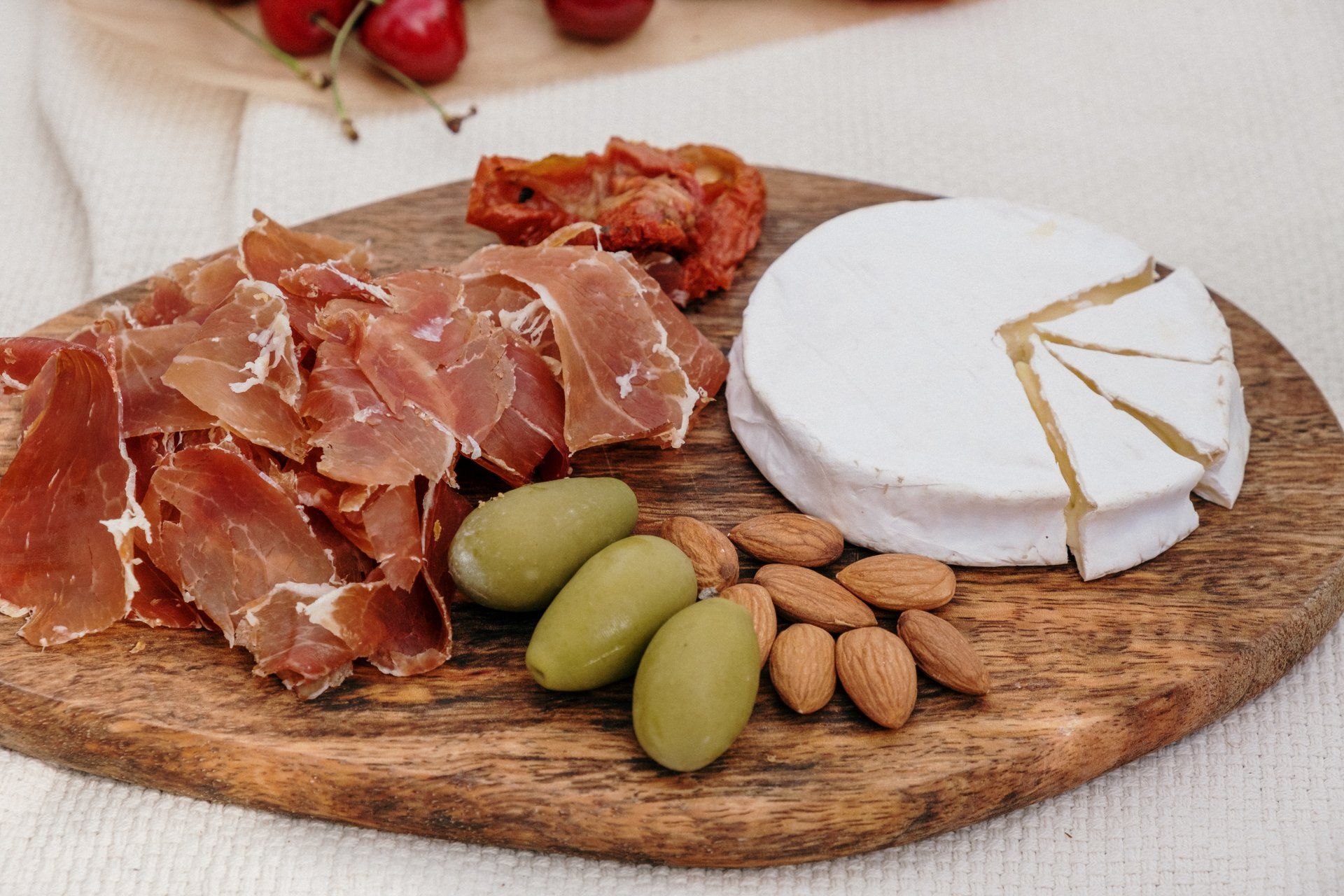 Charcuterie board with sliced prosciutto, brie, olives, almonds, and sun-dried tomatoes.