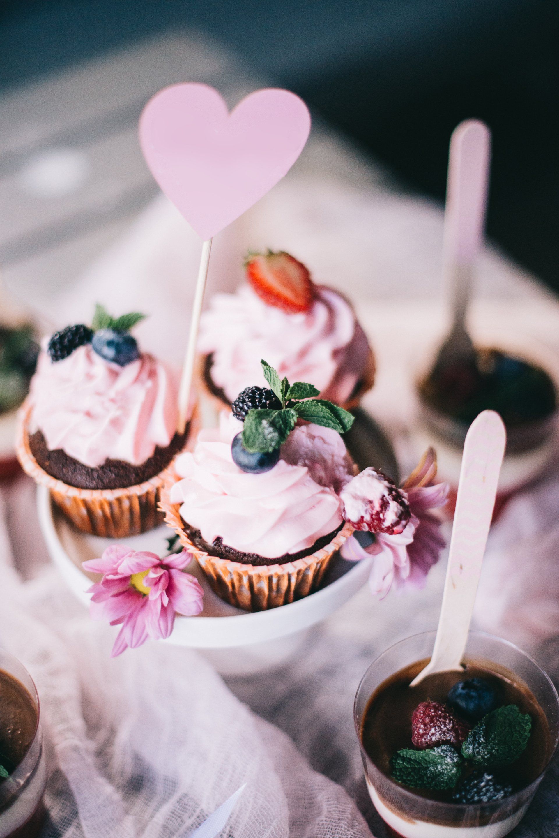 A bunch of cupcakes with pink frosting and berries on a table.