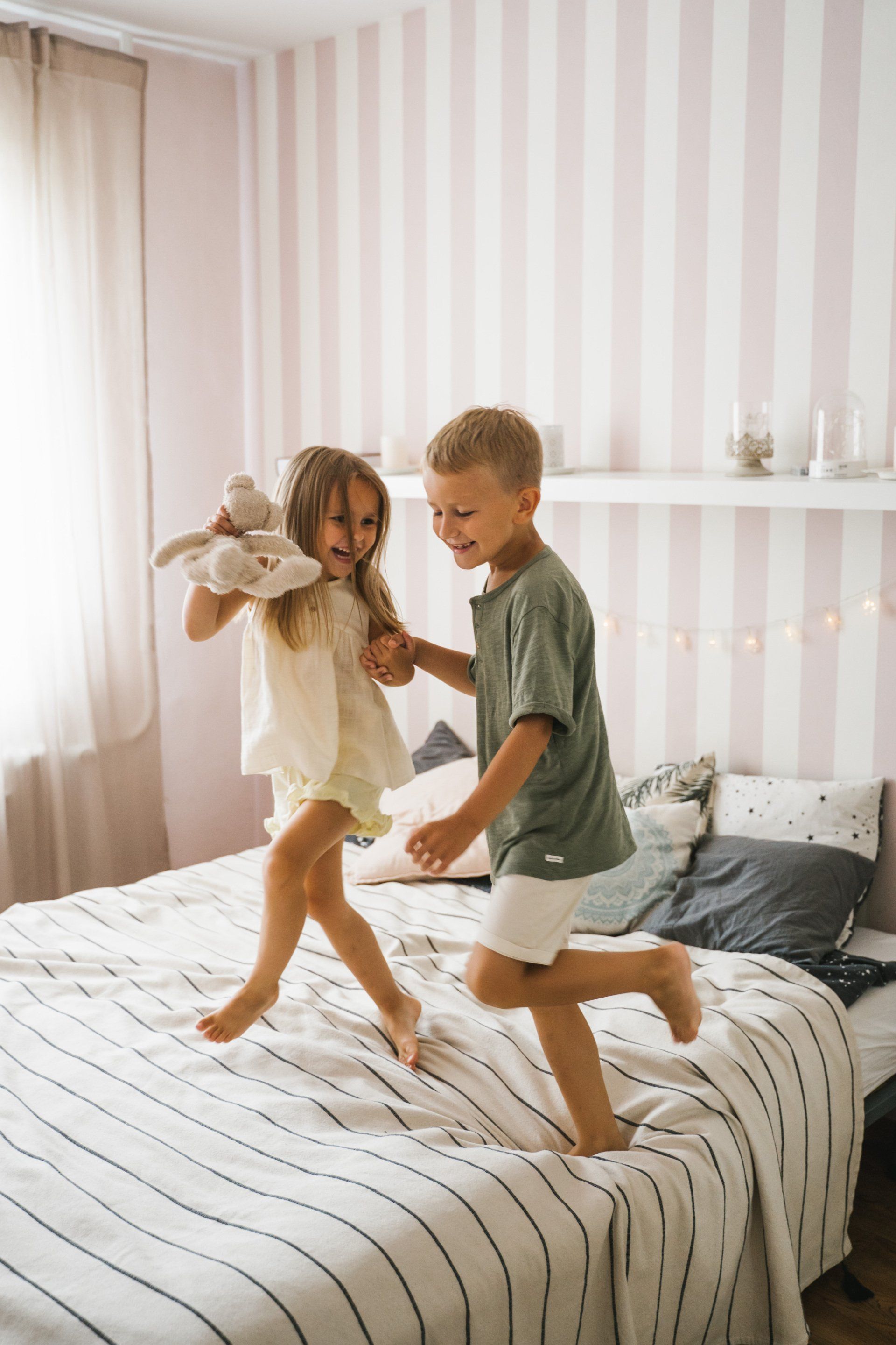 A boy and a girl are jumping on a bed.