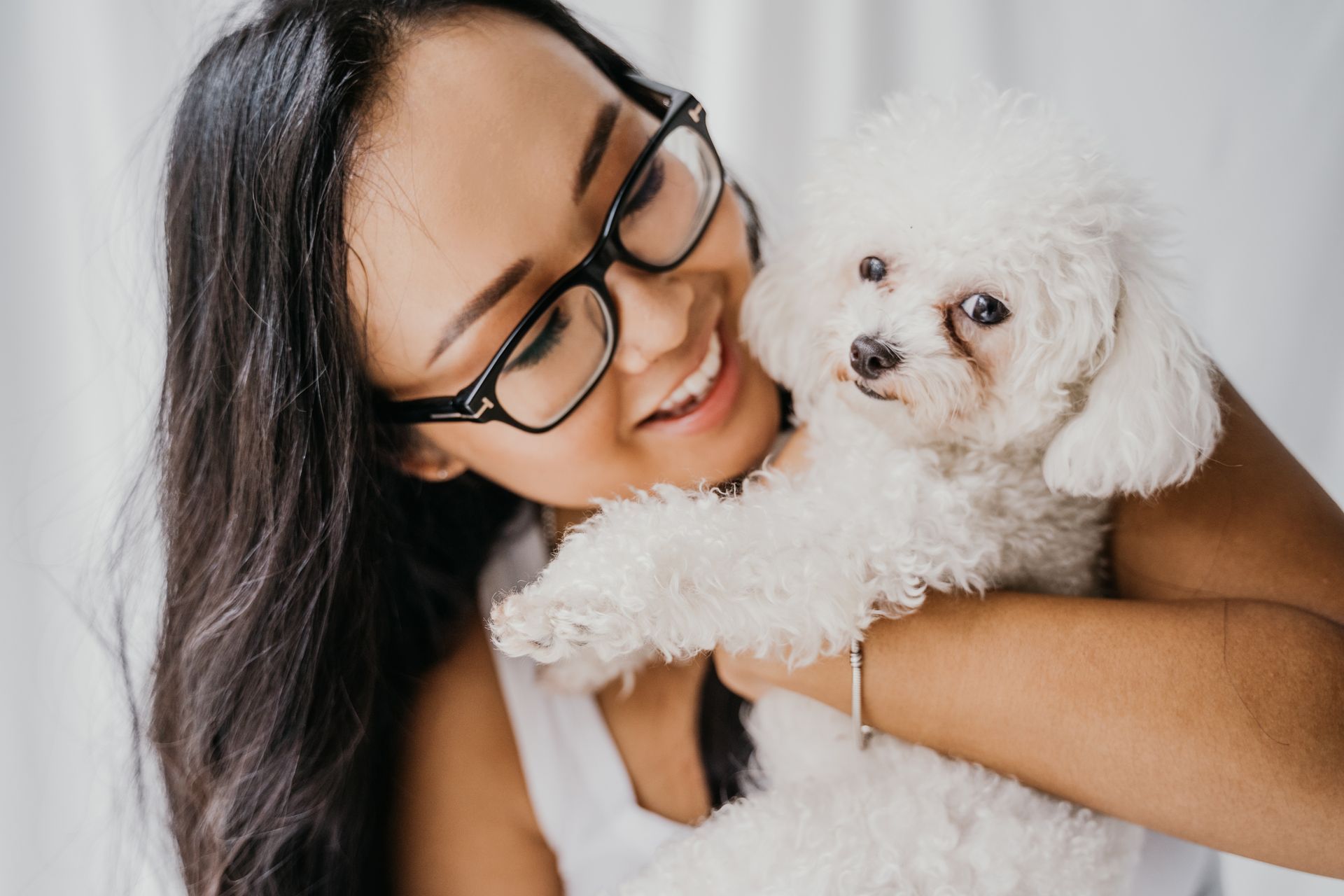 a woman wearing glasses is holding a small white poodle dog .