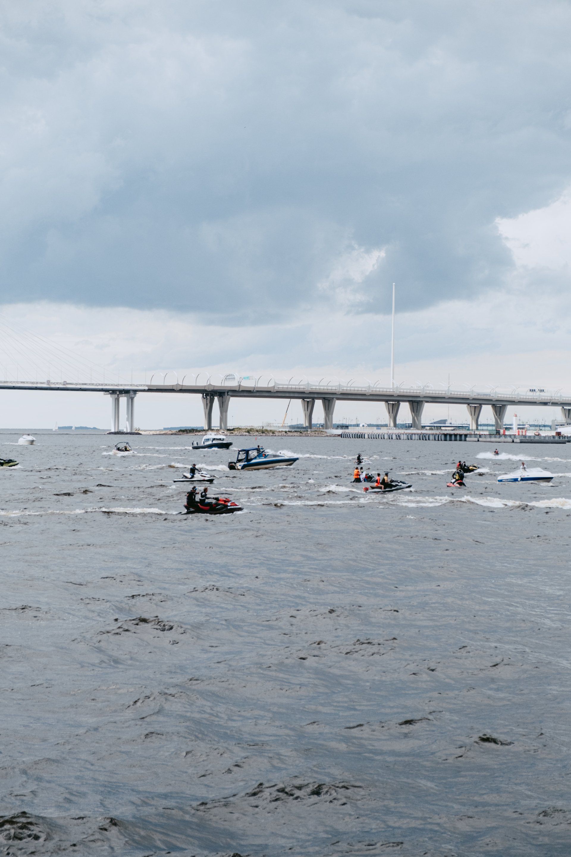 Boats on choppy water near a bridge under a cloudy sky.