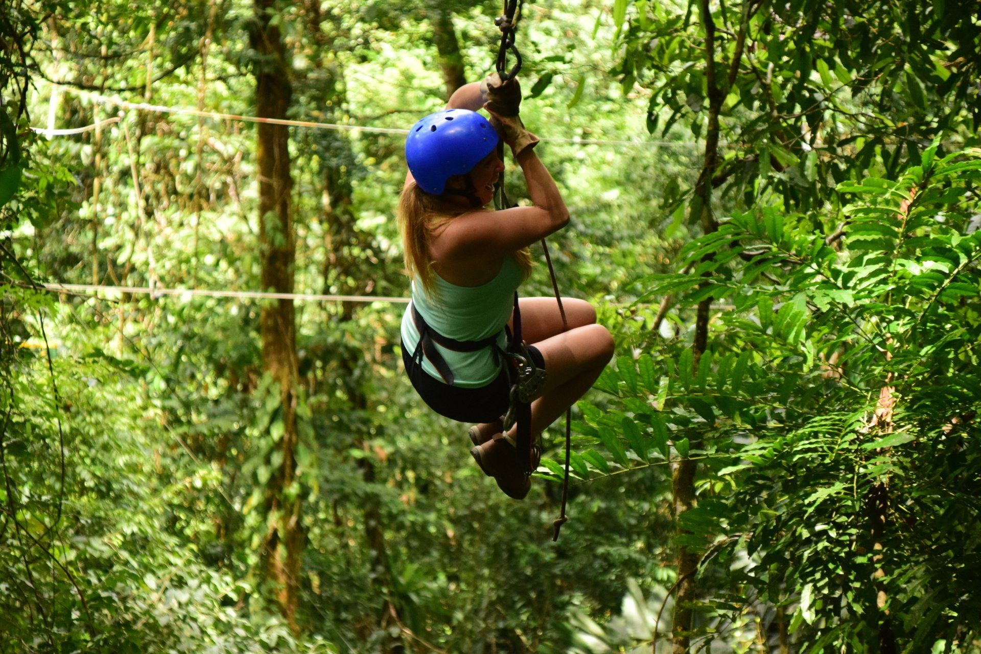 A woman is flying through the air on a zip line in the jungle.