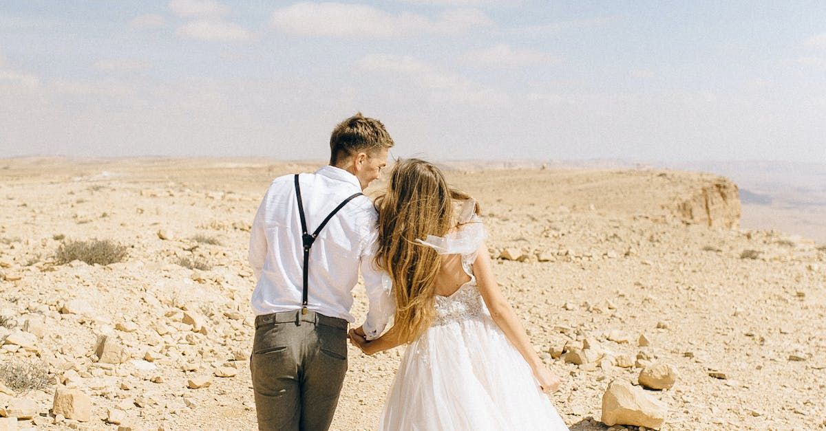 Wedding Couple in Desert Scape on Wedding Day with backs to camera, walking away, hand in hand.