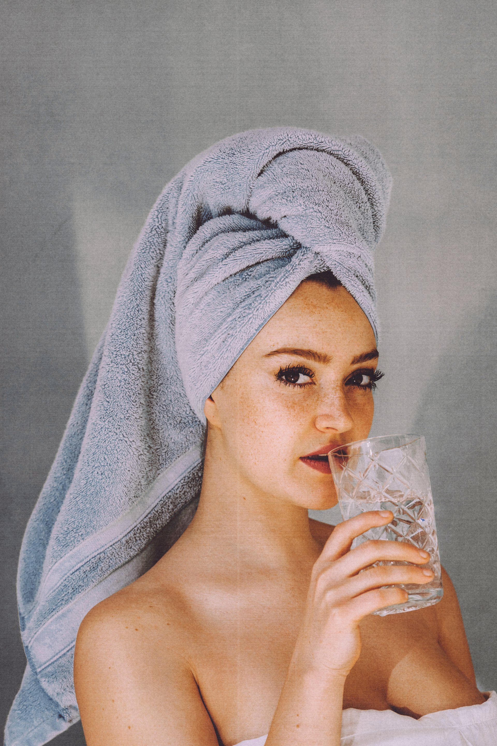 woman holding a glass of water with a towel wrapped around her hair