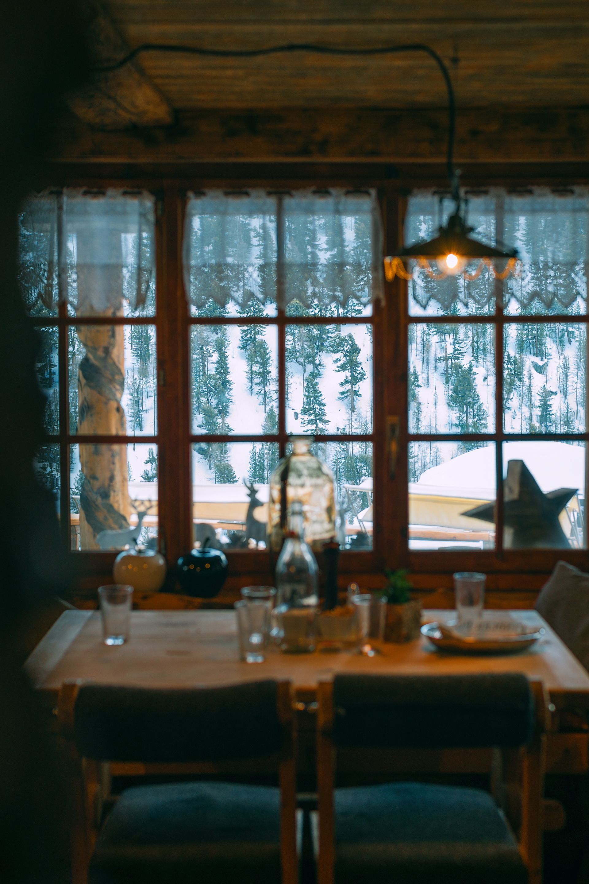 a table and chairs in front of a sash window with a view of a snowy forest .