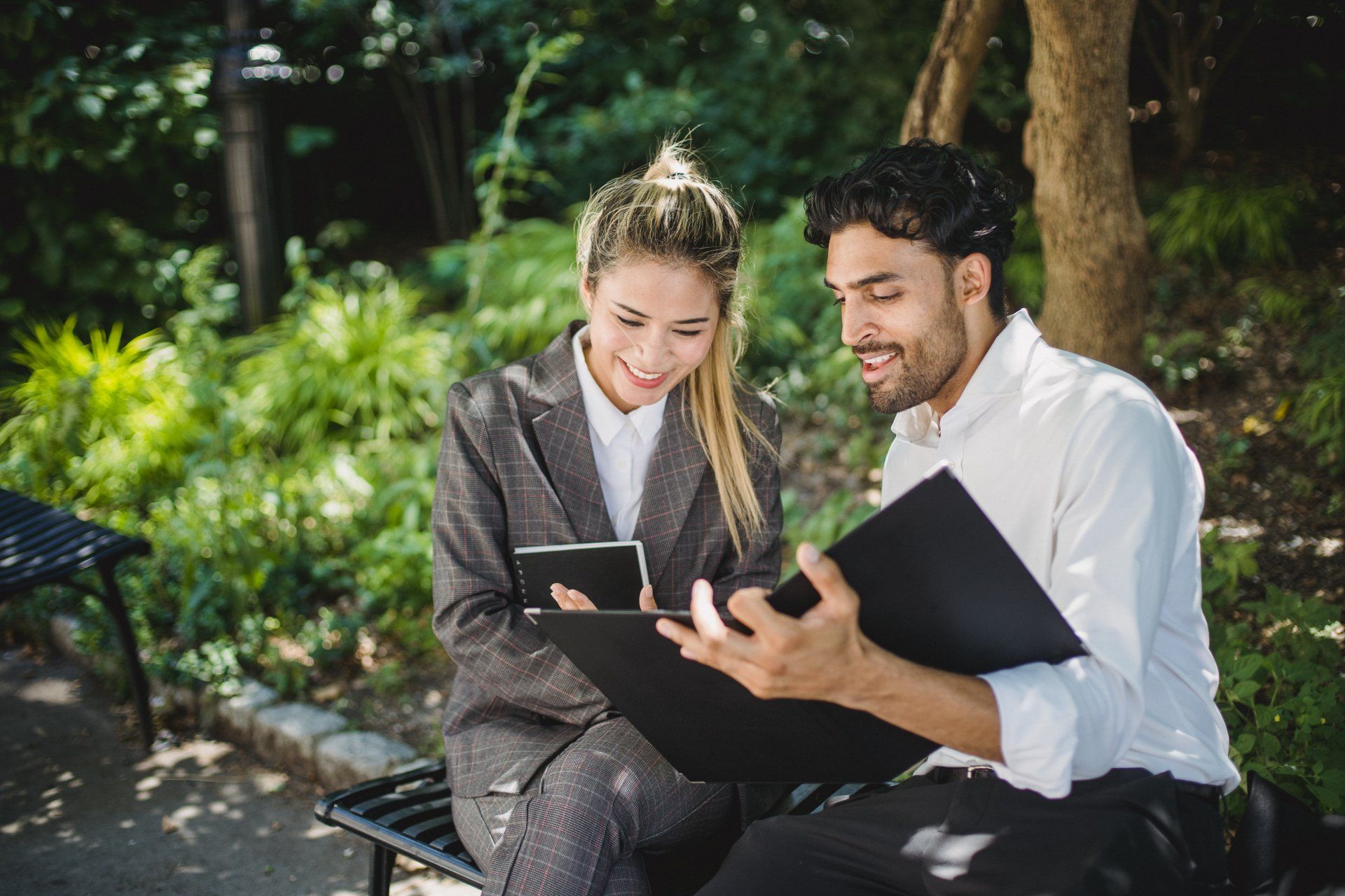 A man and a woman are sitting on a bench looking at a tablet.