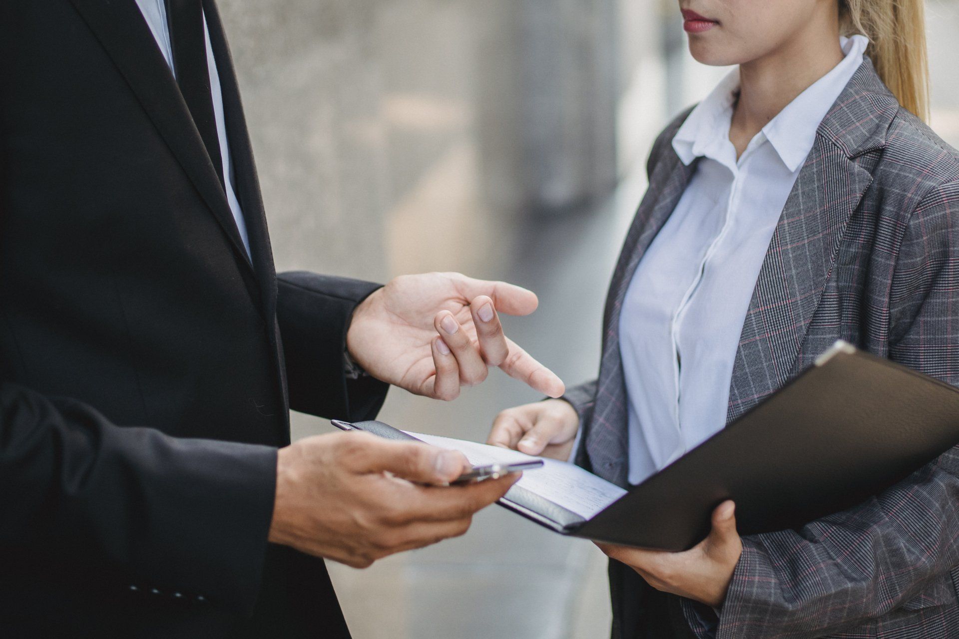 A man is holding a cell phone and a woman is holding a clipboard.