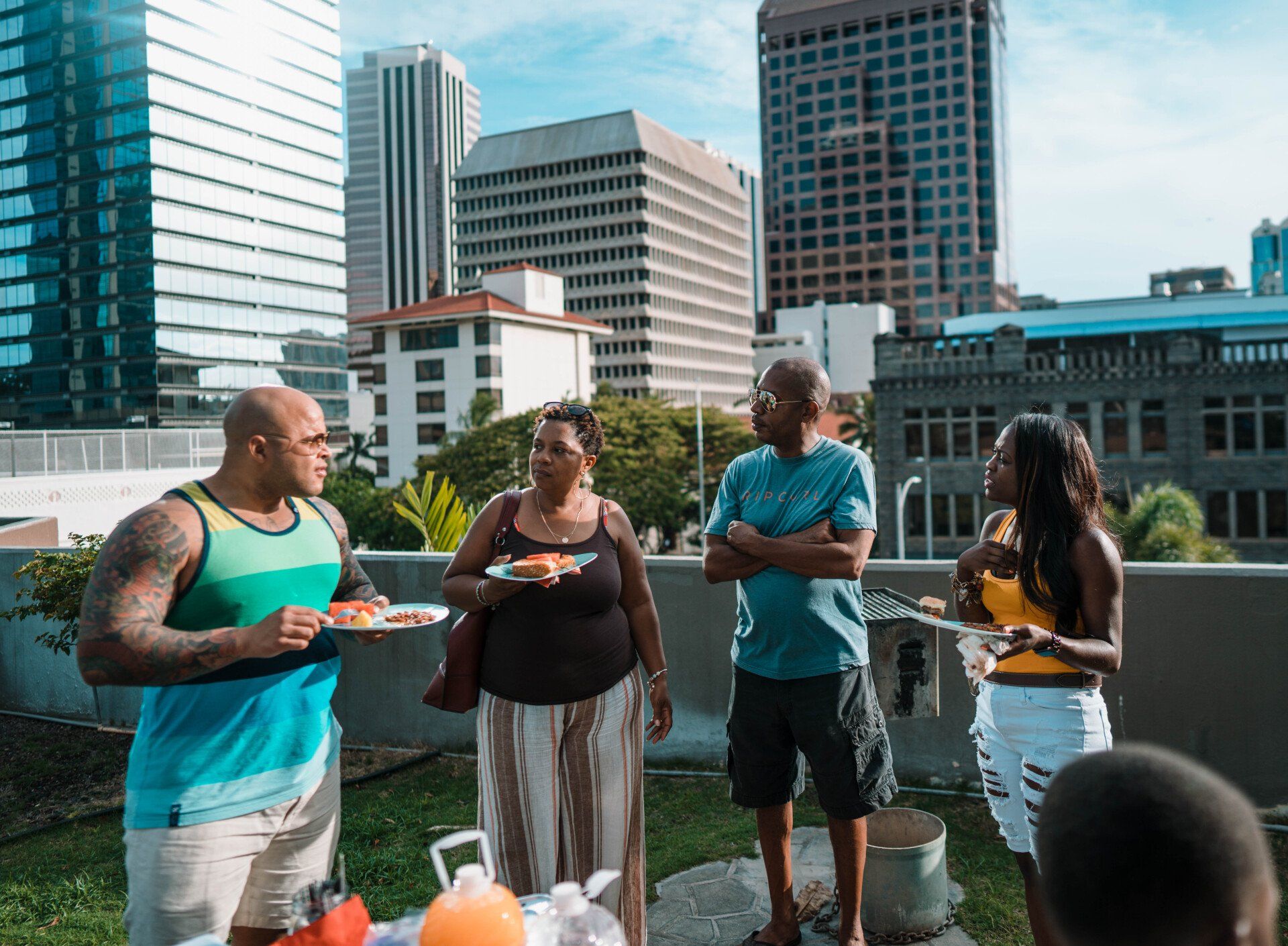 Four black coworkers eating on the top of a building with high rise buildings in the background