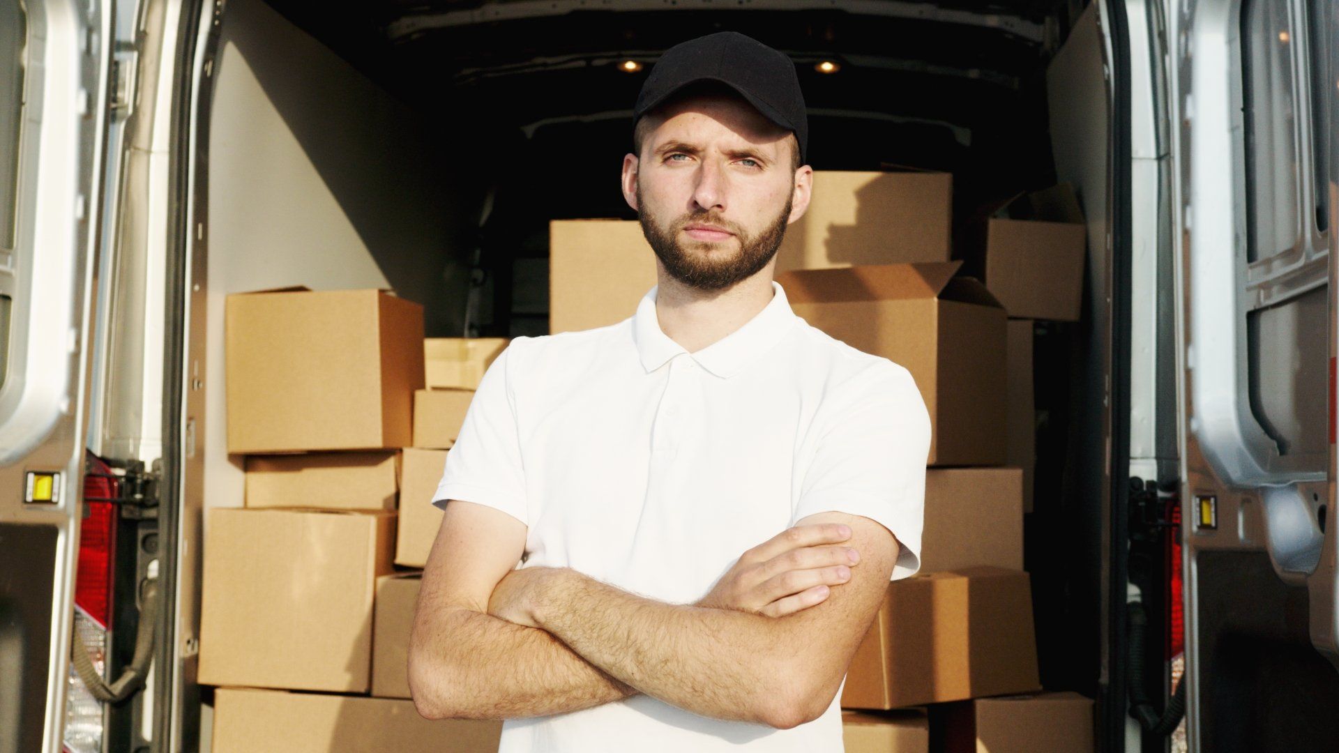 A man is standing in front of a van filled with cardboard boxes.