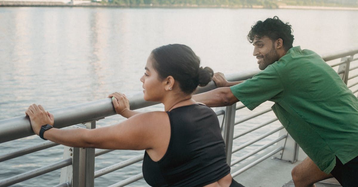 A man and a woman are stretching on a railing overlooking the water.