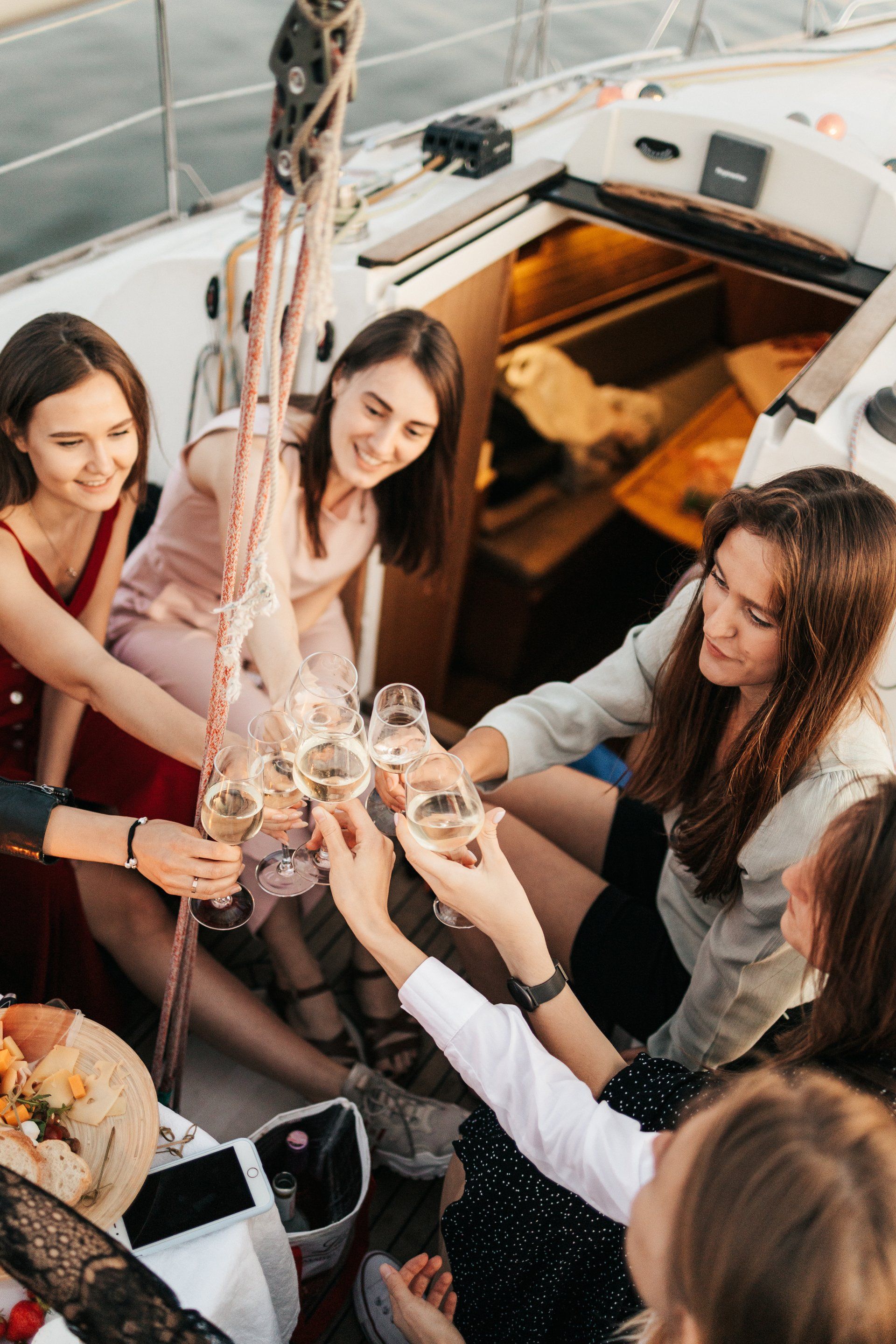 A group of women are sitting on a boat toasting with champagne glasses.