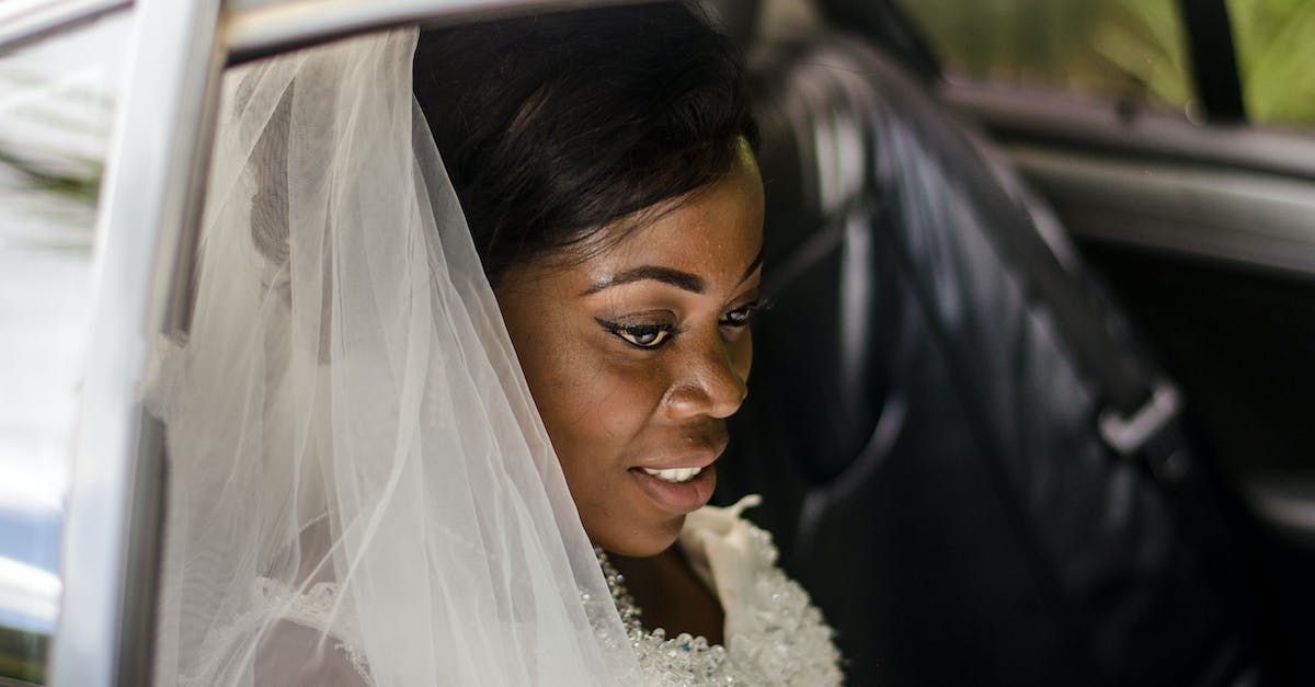 A bride in a veil is sitting in the back seat of a car.