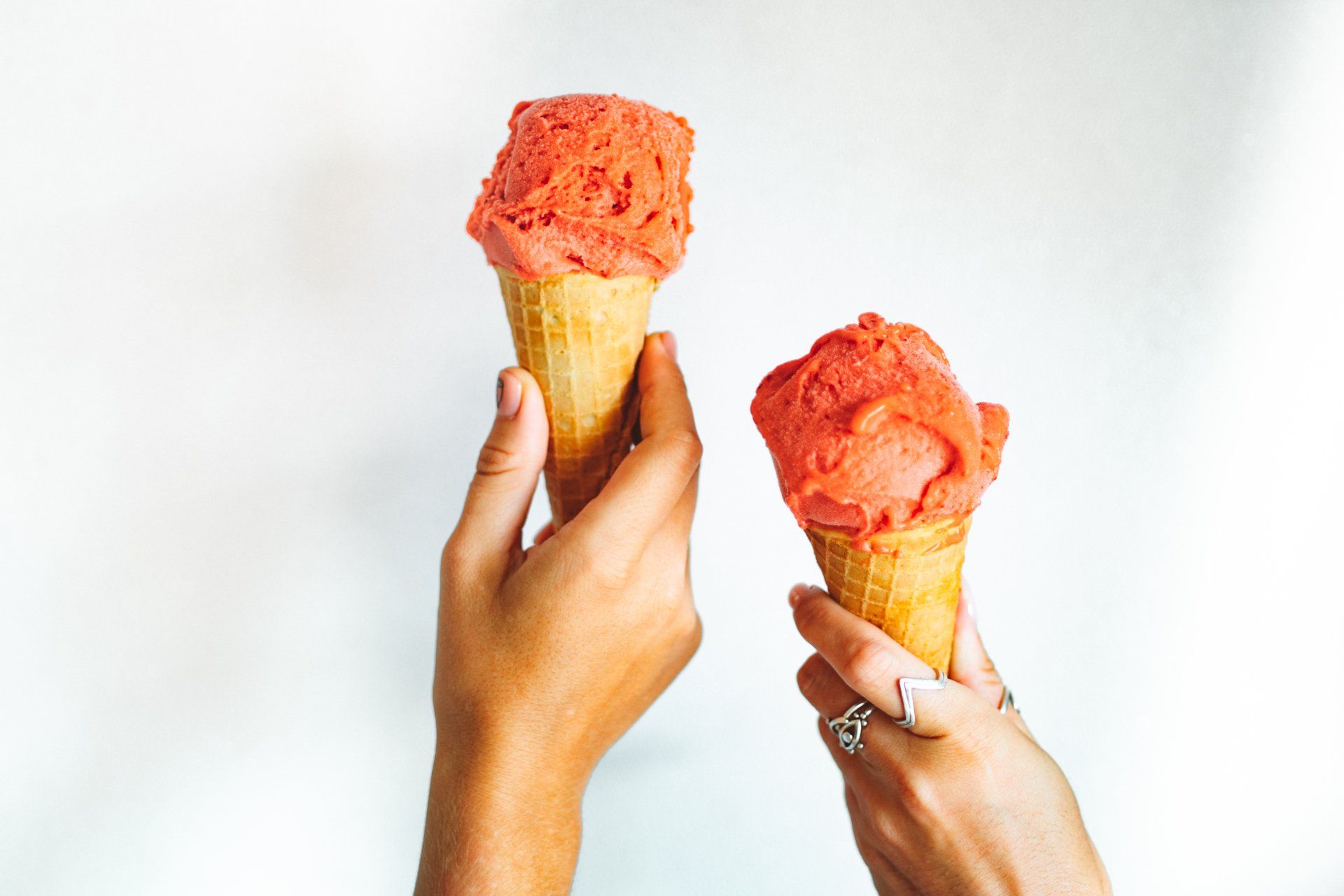 Two hands held against a white background, each holding a waffle cone topped with a scoop of orange sorbet or ice cream.