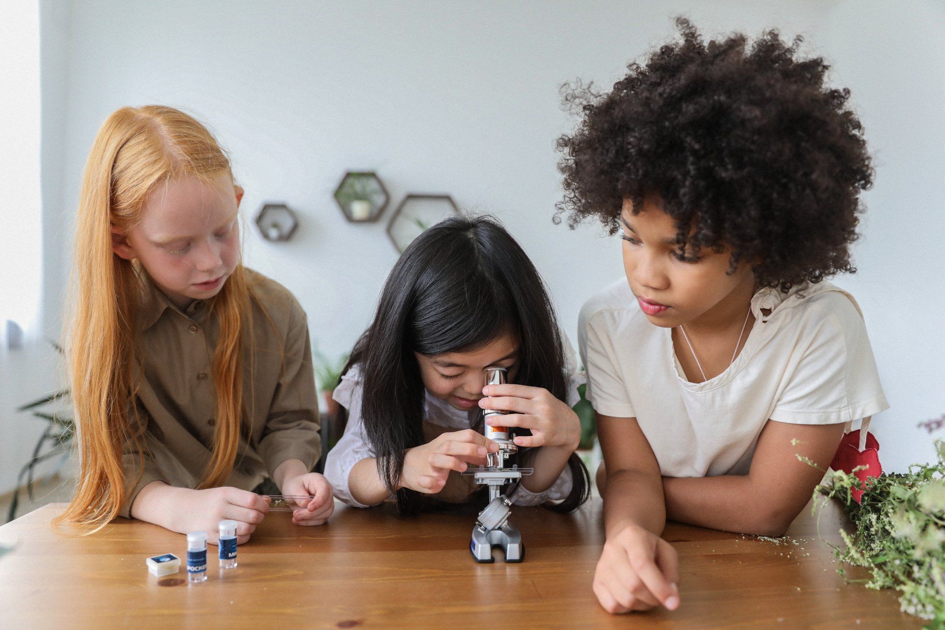 A group of children are sitting at a table looking through a microscope.