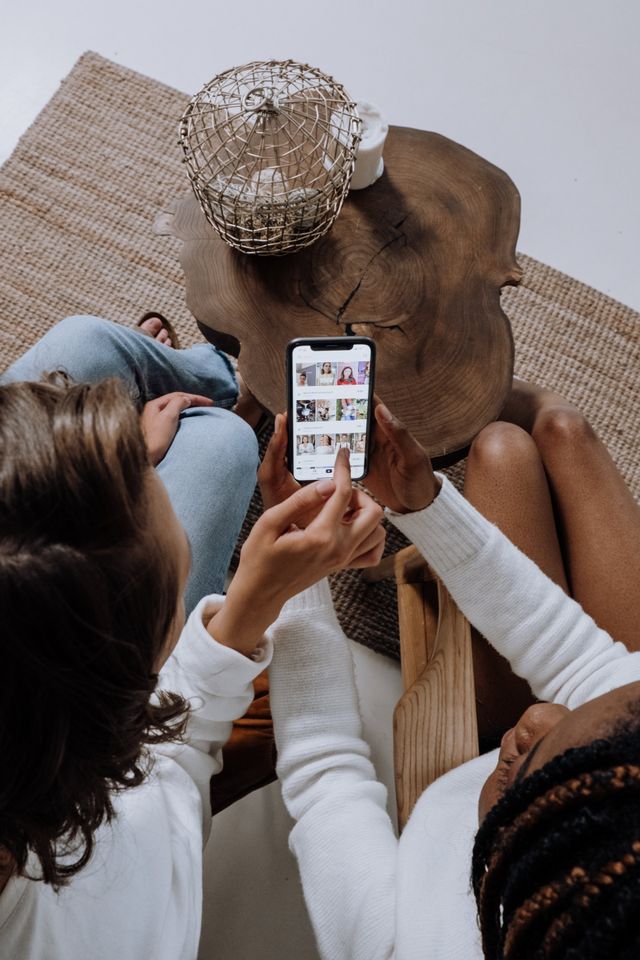 Two women are sitting on a couch looking at a cell phone.