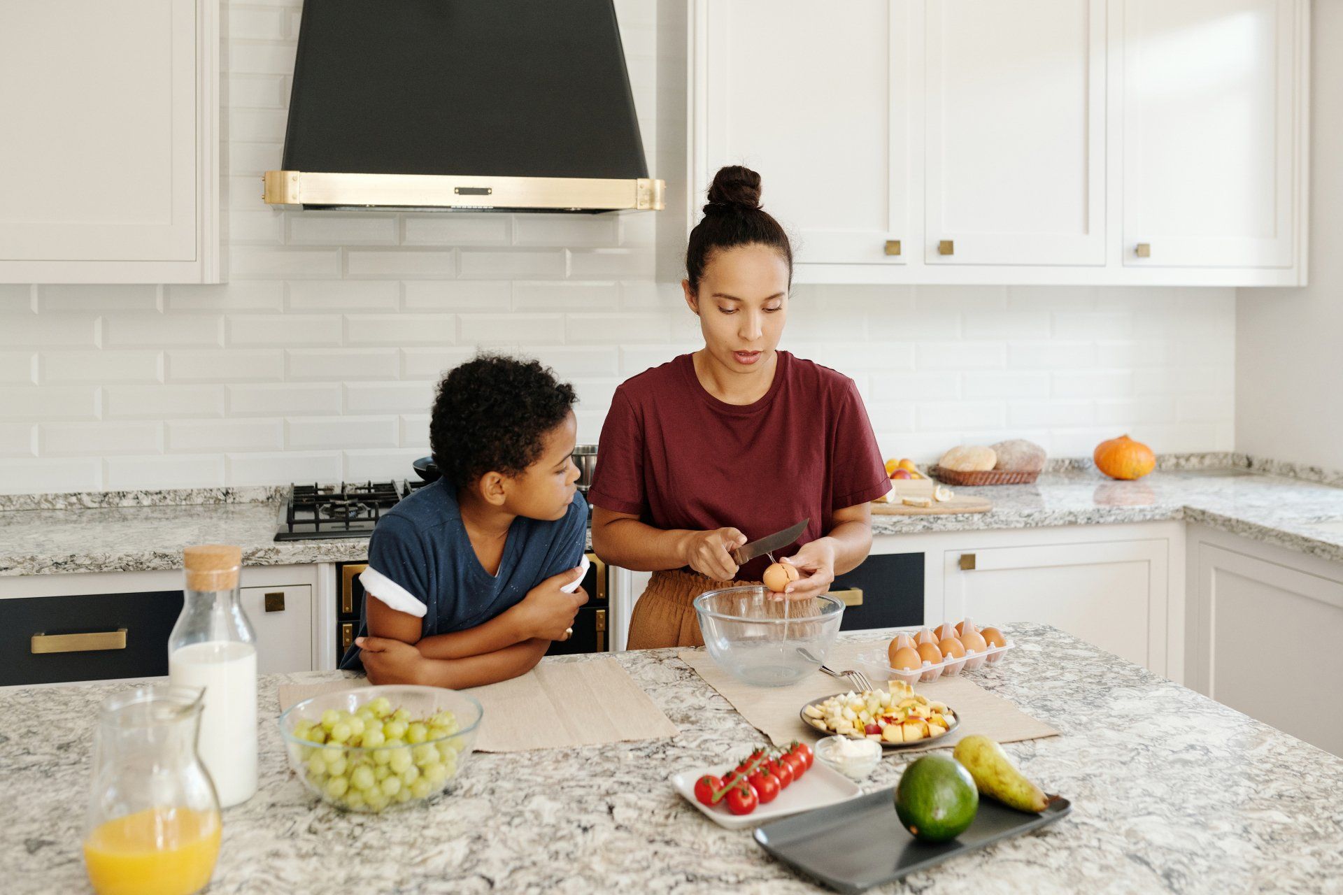 A woman and a boy are sitting at a table in a kitchen preparing food.
