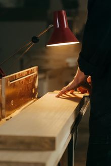 A person is cutting a piece of wood on a table under a lamp.