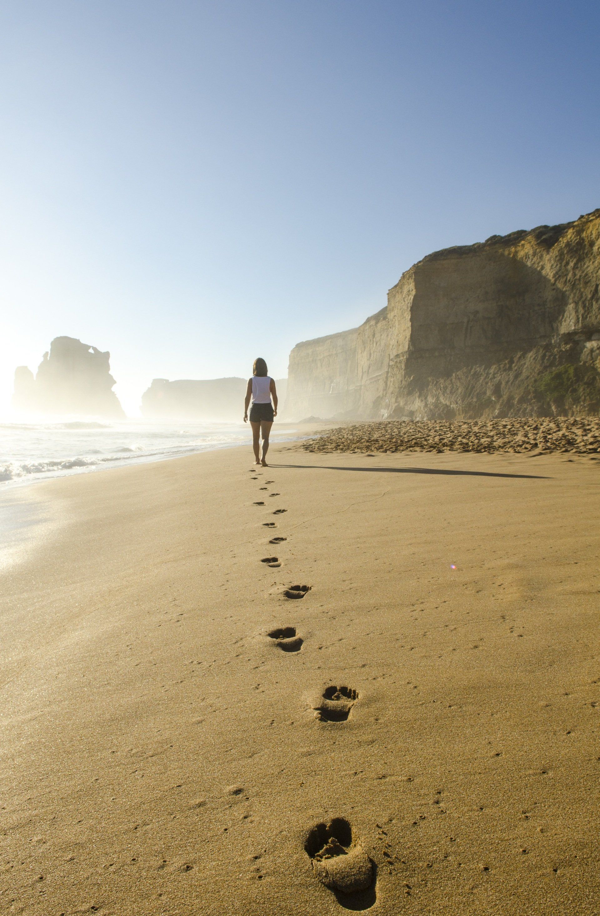 A woman is walking along the beach leaving footprints in the sand.
