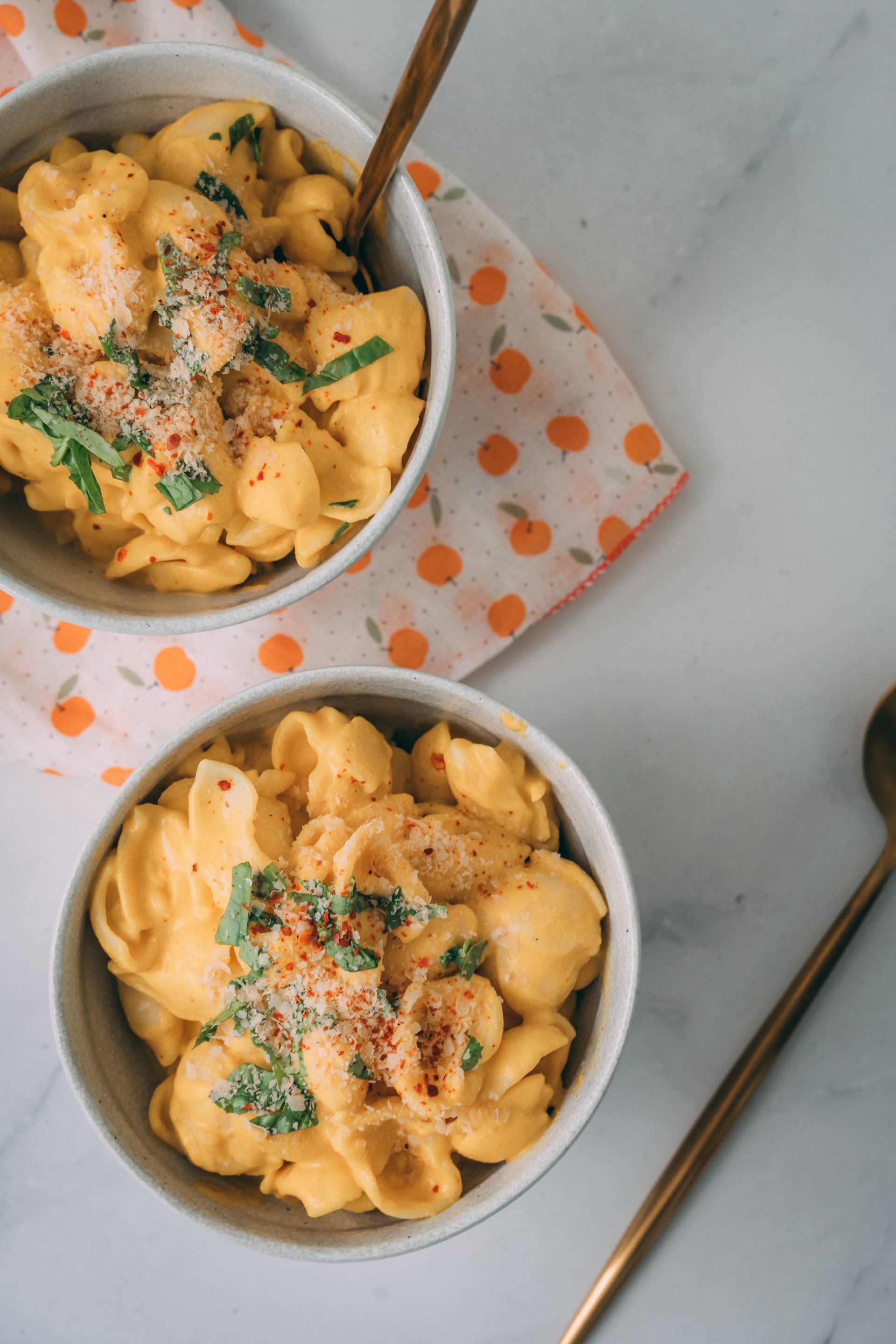 Two bowls of macaroni and cheese with spoons on a table.