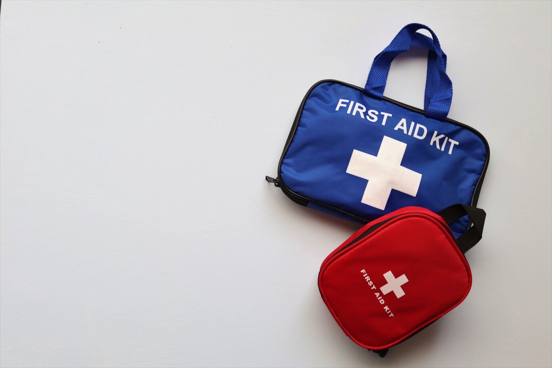 A blue first aid kit and a red first aid kit are on a white surface.