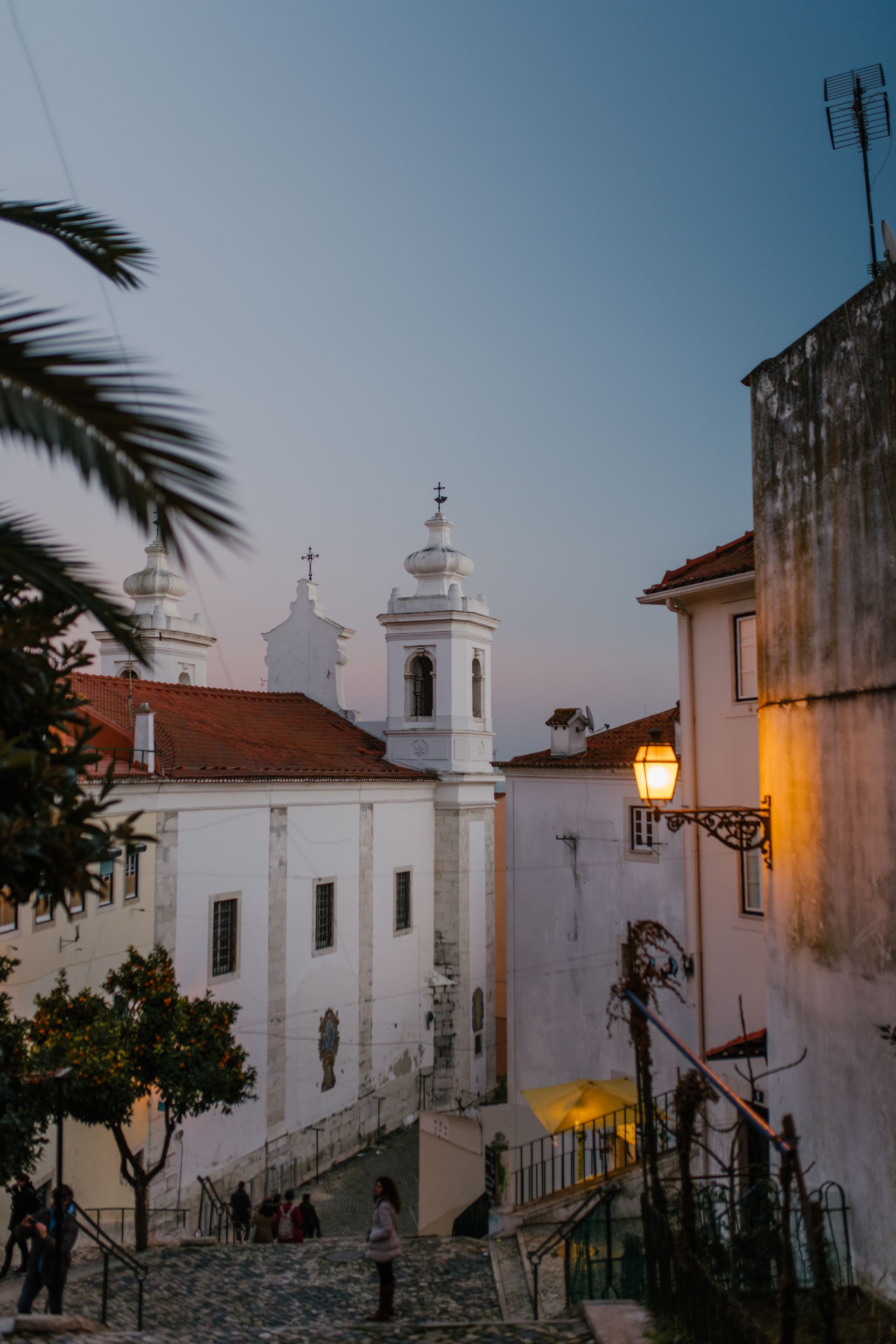 A narrow street with a church in the background and a palm tree in the foreground.