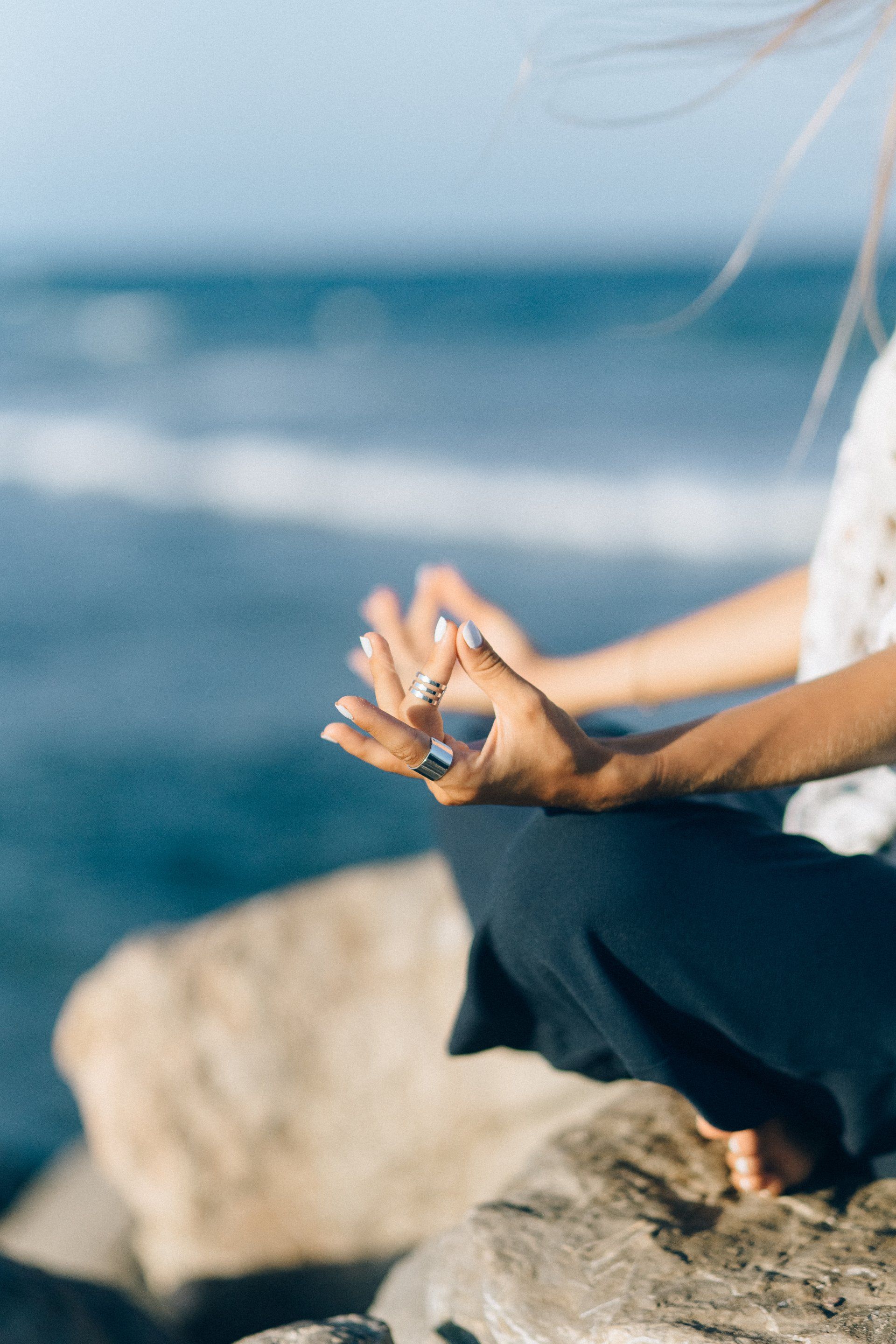 A woman is sitting on a rock near the ocean meditating.