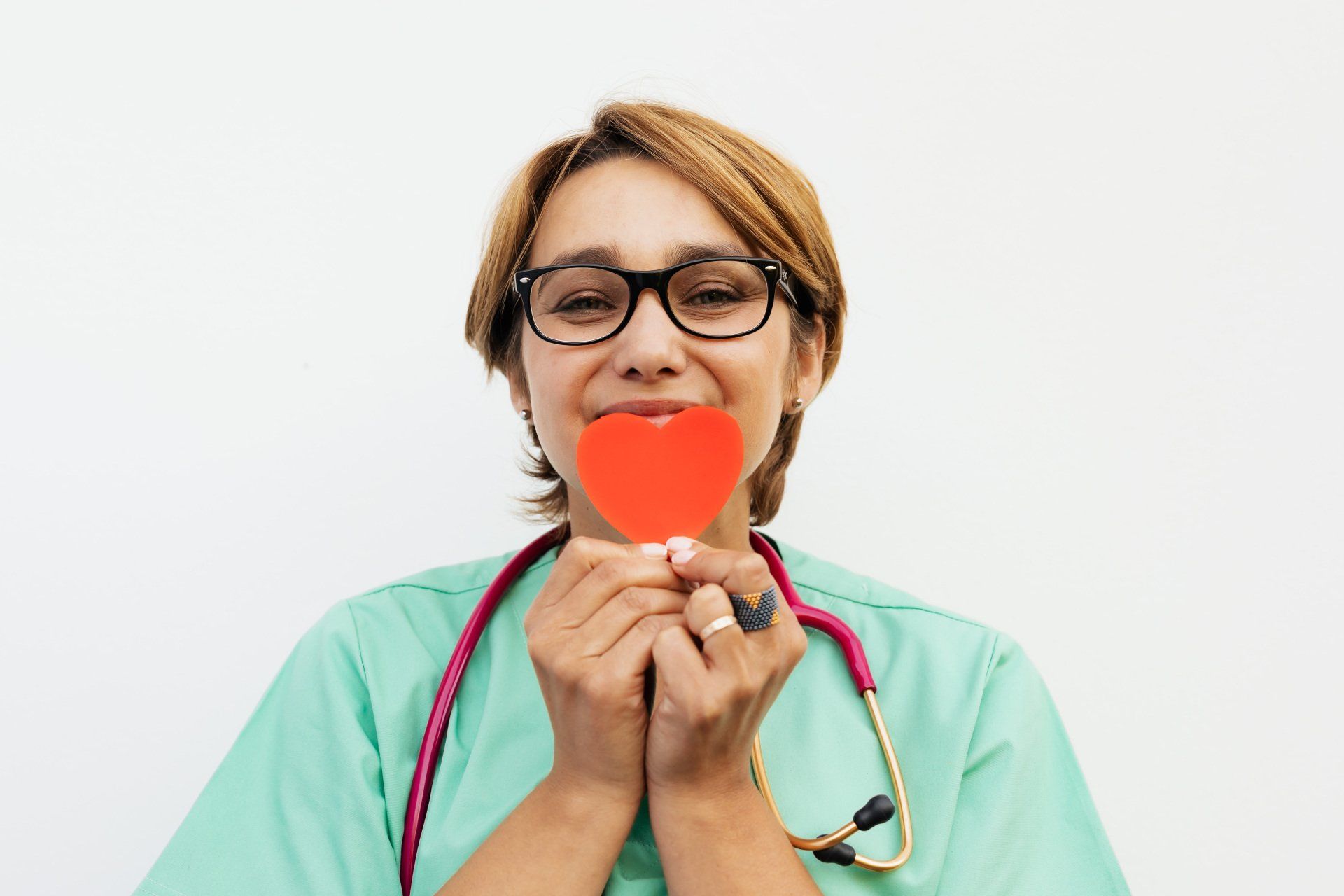 A female doctor is holding a red heart in front of her face.