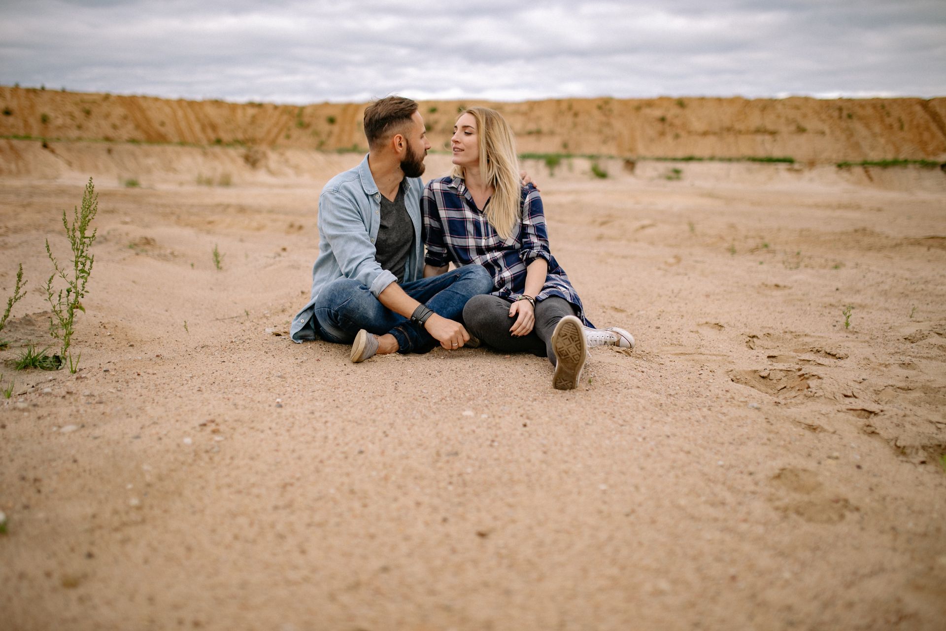 A man and a woman are sitting on the ground in the desert looking at each other.