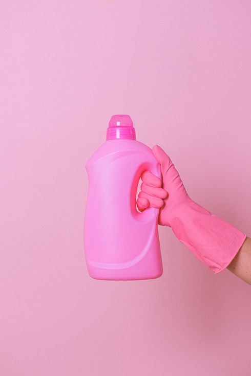 A person wearing a pink rubber glove is holding a pink bottle of laundry detergent.