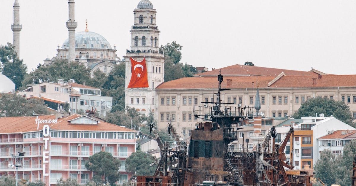 Stadtbild mit einer türkischen Flagge, die von einem weißen Turm weht, Booten und Gebäuden.