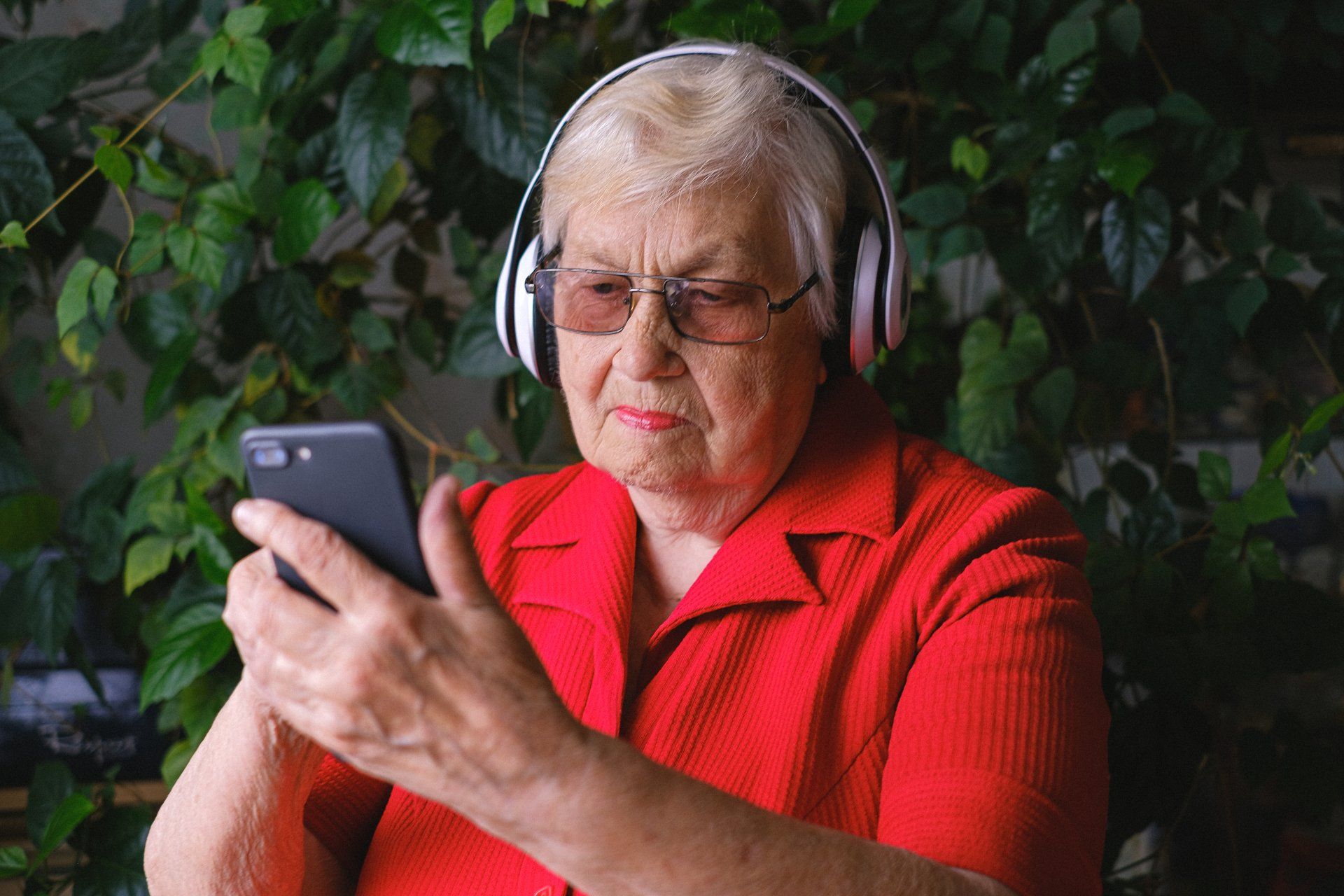 An elderly woman wearing headphones is using a cell phone.