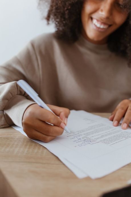 A woman is sitting at a table writing on a piece of paper.