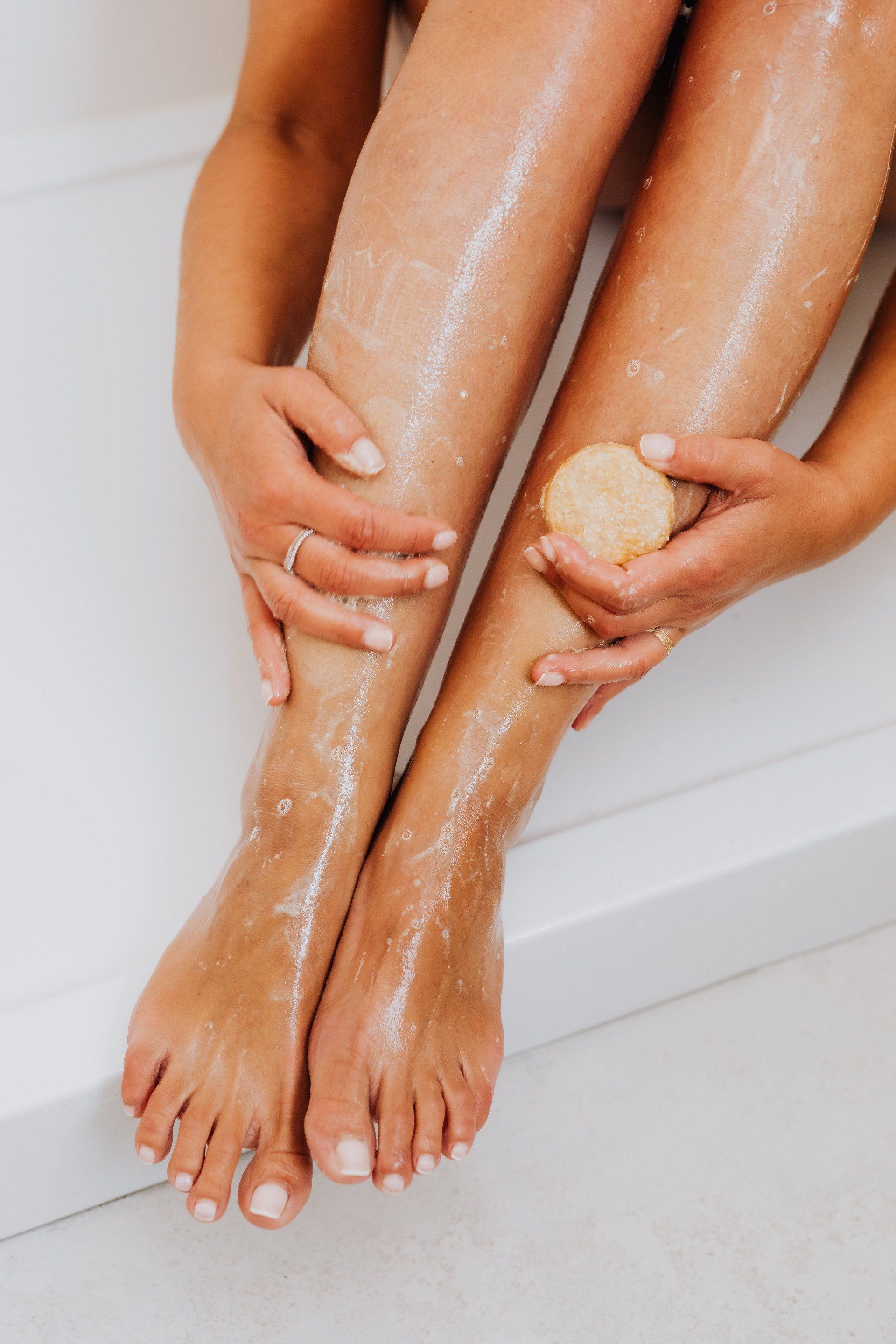 A woman is sitting in a bathtub washing her legs with a sponge.