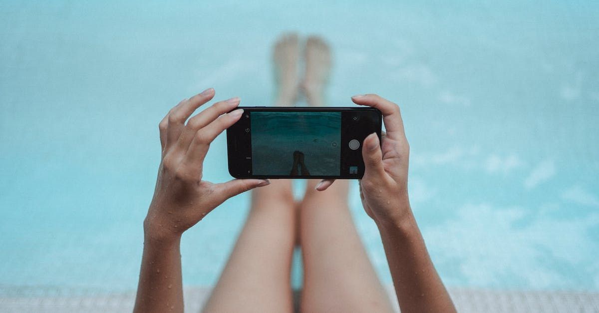 A woman is taking a picture of her feet in a swimming pool with a cell phone.