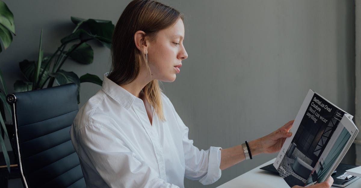 A woman is sitting at a desk reading a magazine.