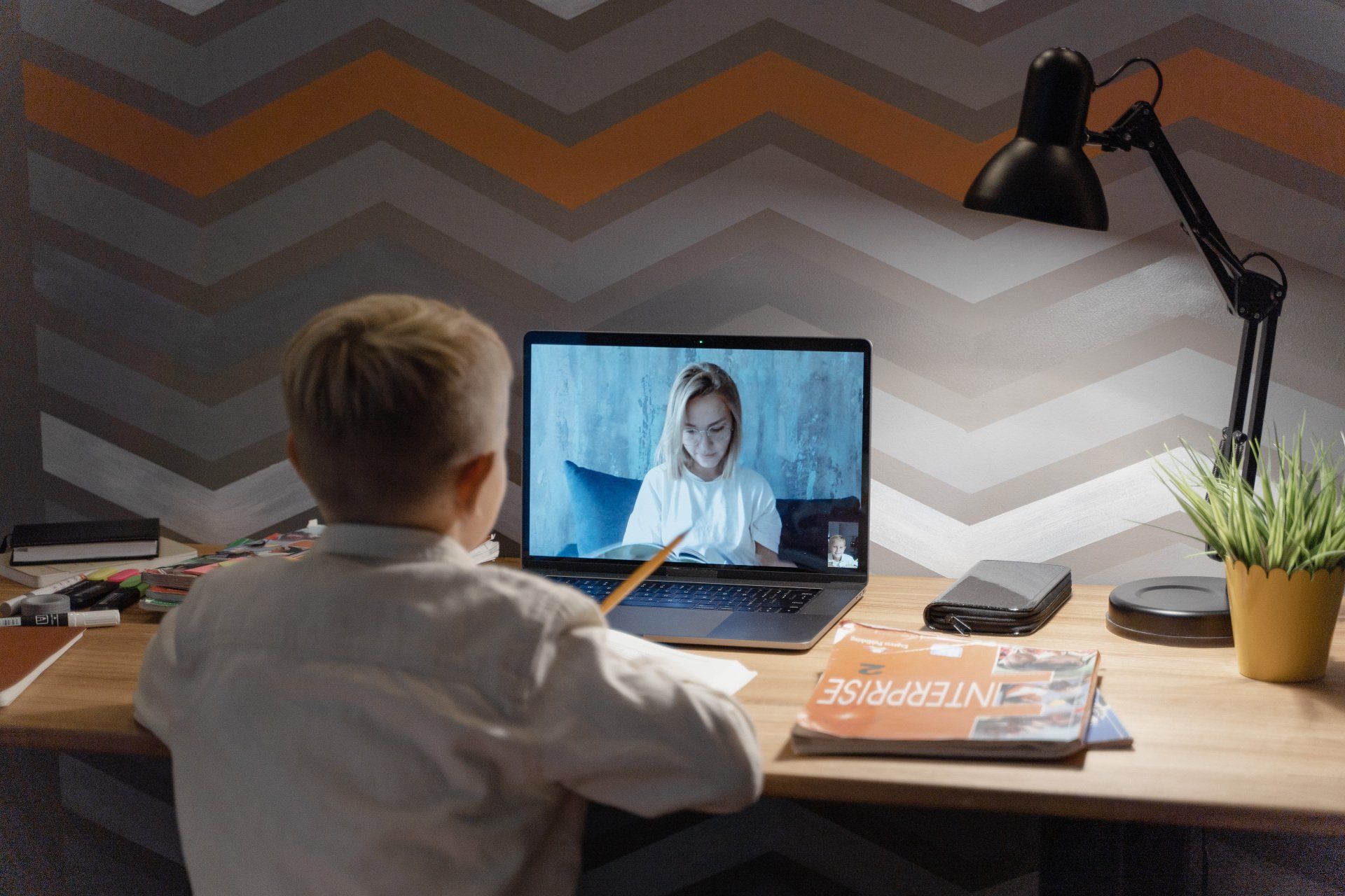 A young boy is sitting at a desk using a laptop computer.