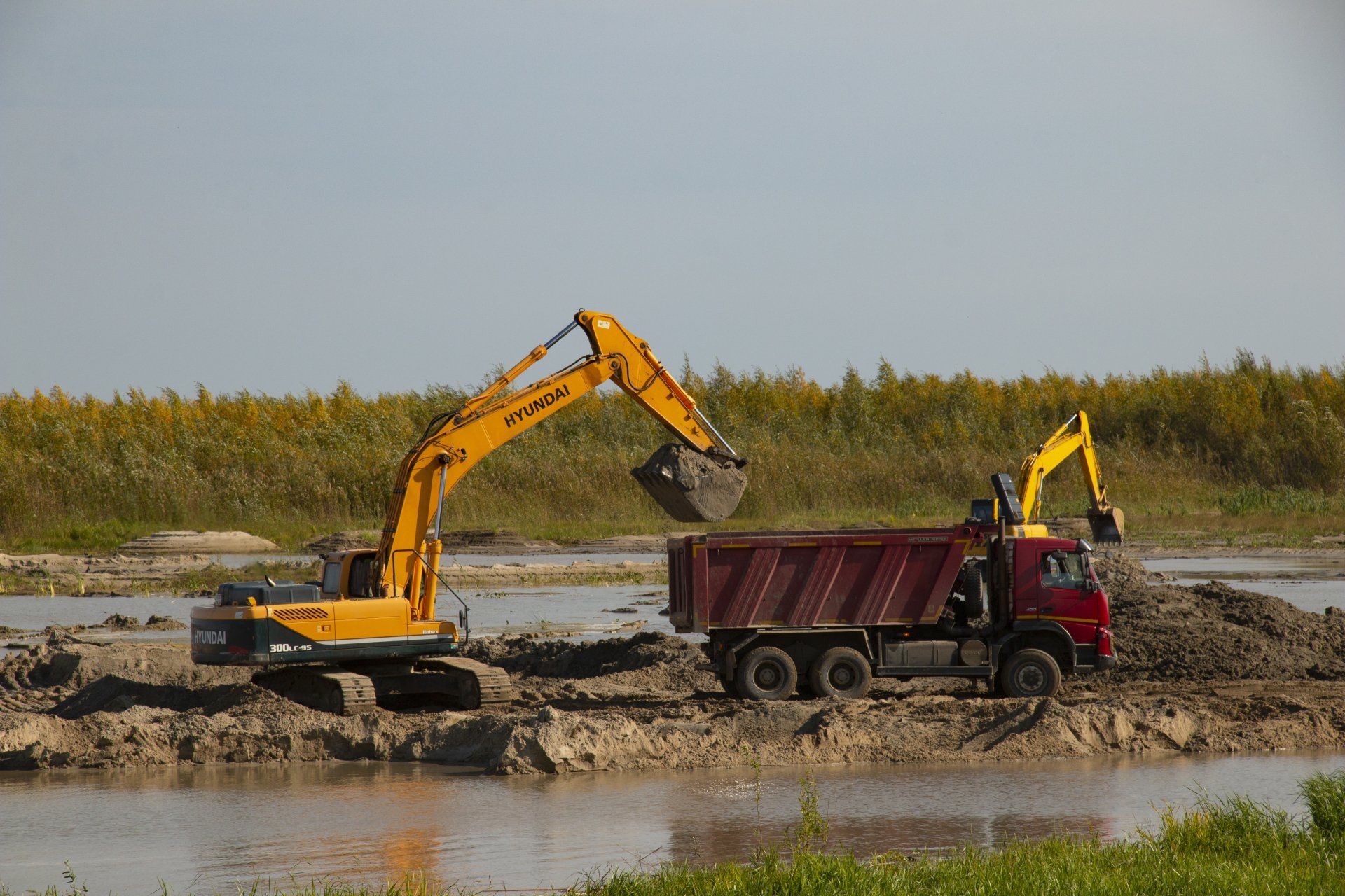 A yellow excavator is loading dirt into a red dump truck.