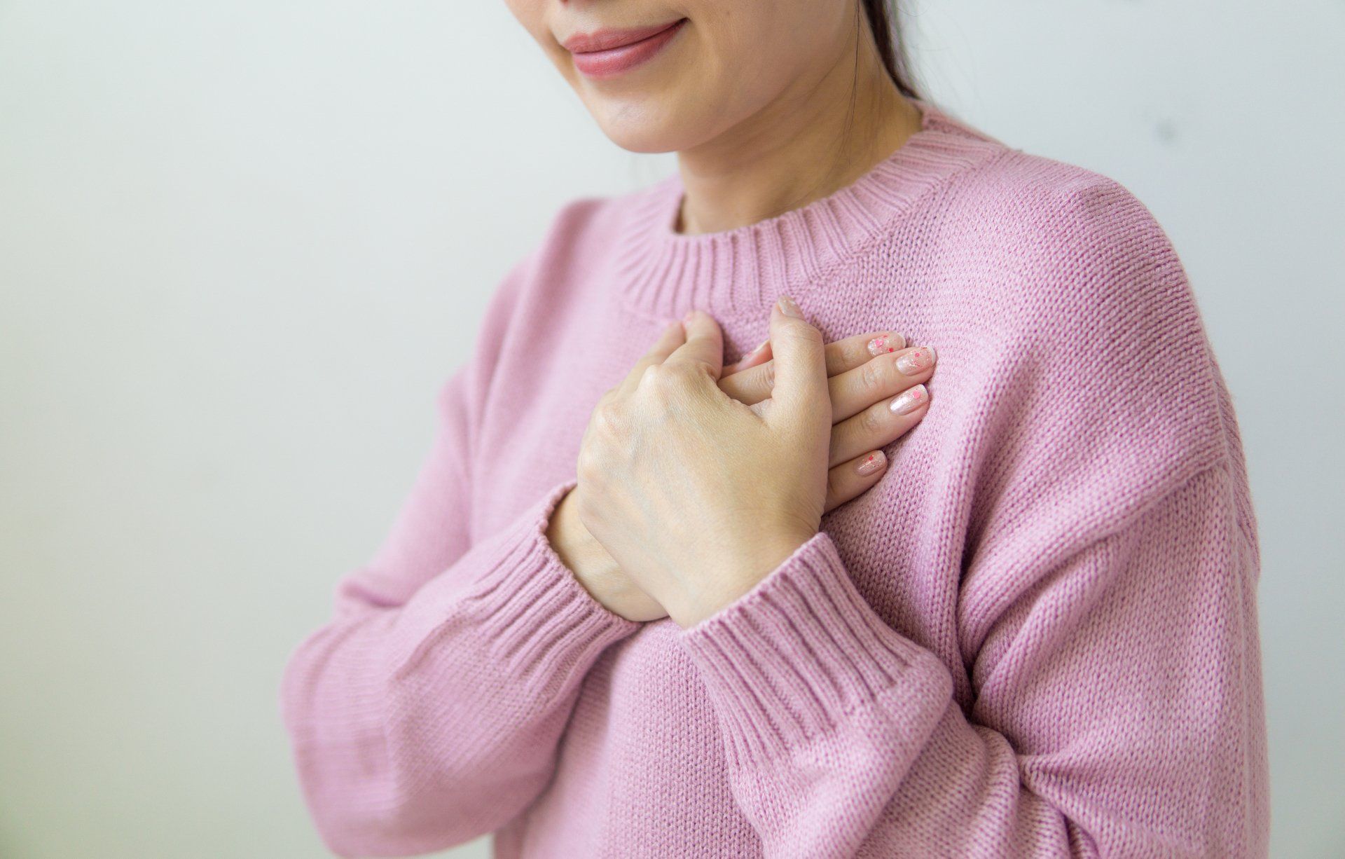 A woman in a pink sweater is holding her hands to her chest.