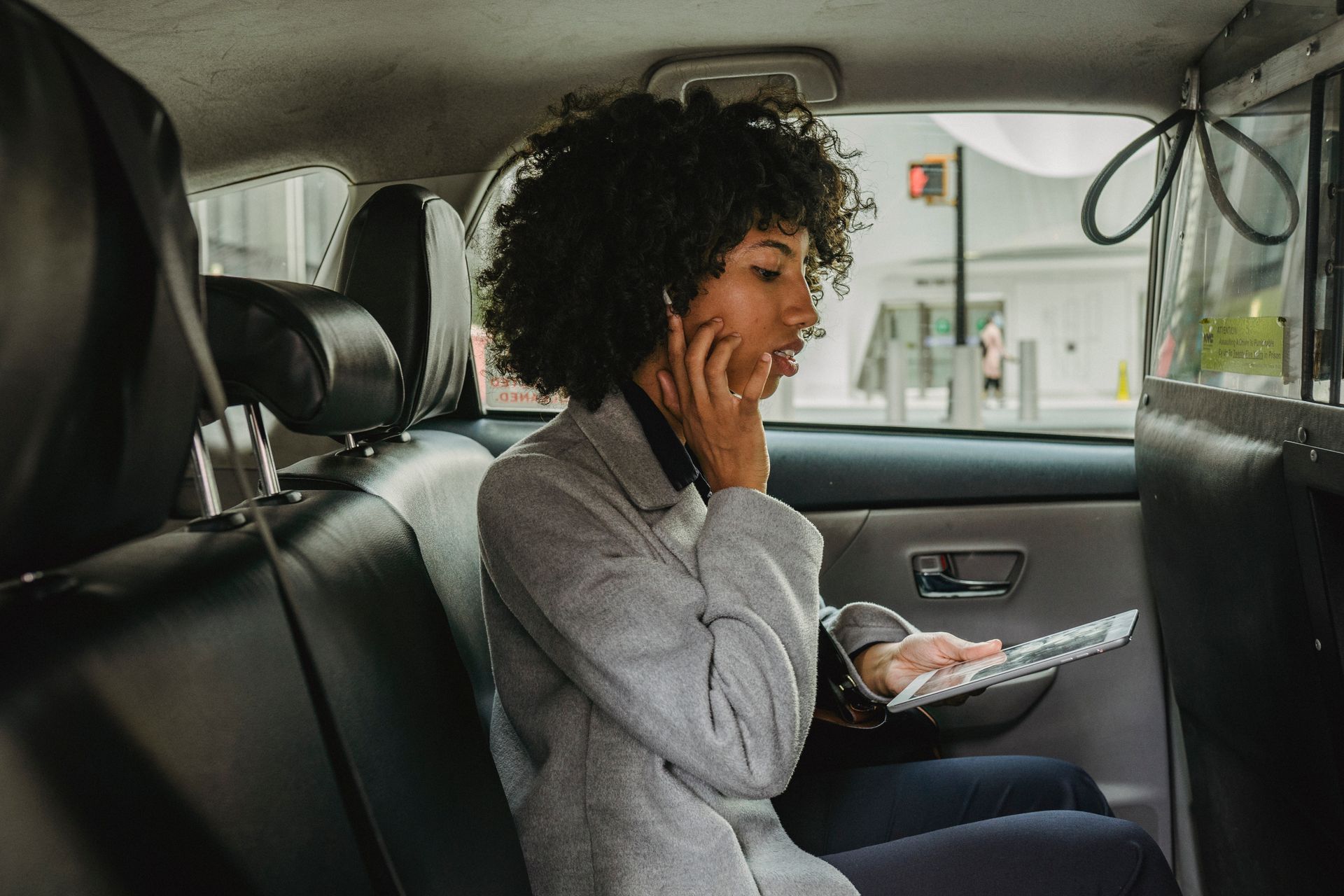 A woman is sitting in the back seat of a car using a laptop and talking on a cell phone.