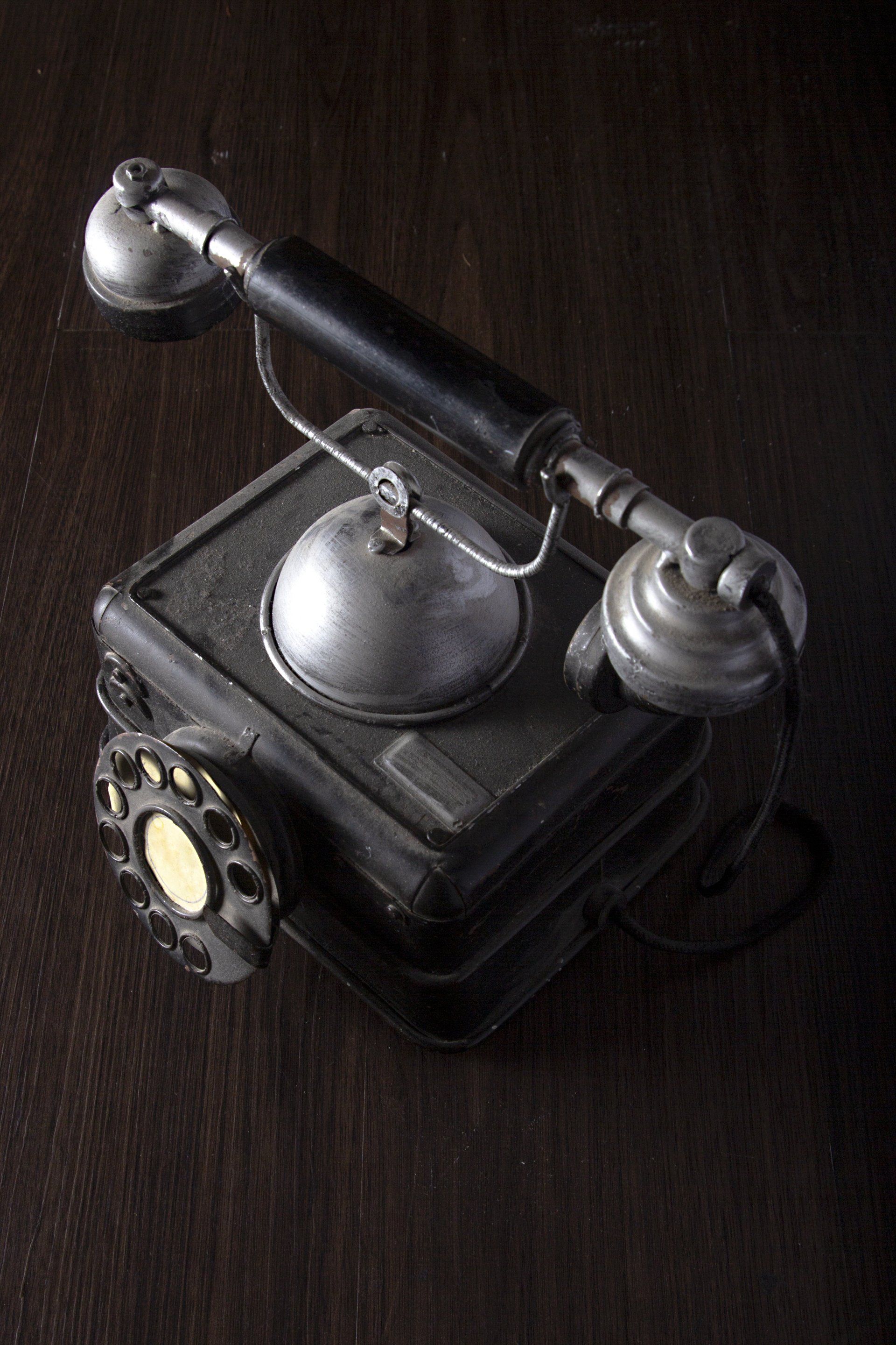 A free standing, old dark grey phone with a rotary dial on top of a desk