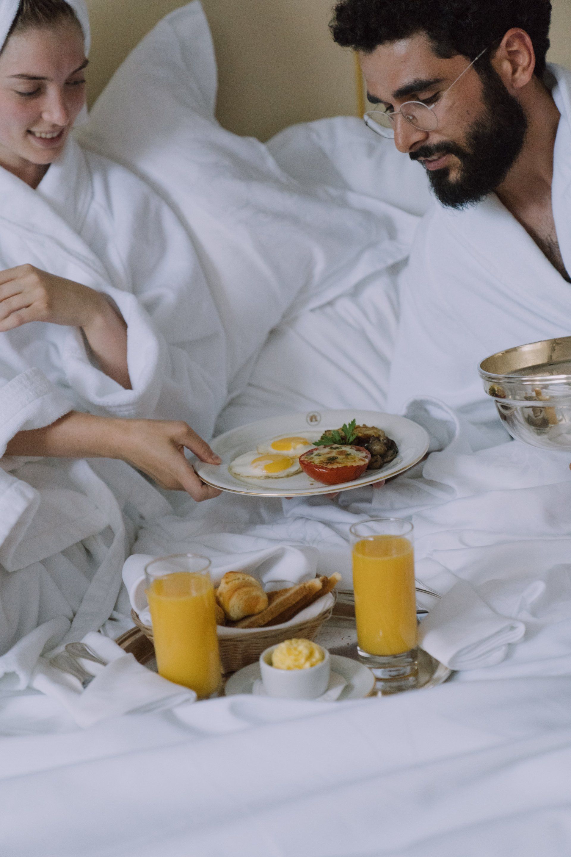 A man and a woman are laying in bed with a tray of food.
