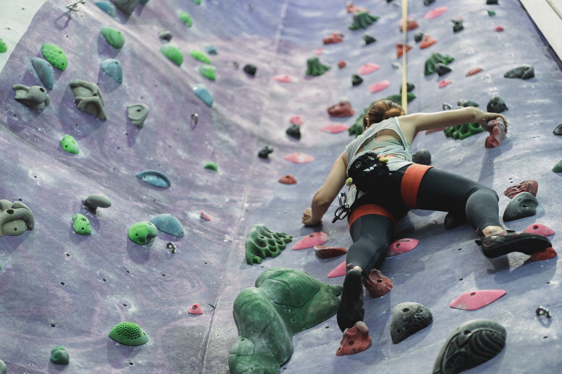 A woman is climbing up a climbing wall.