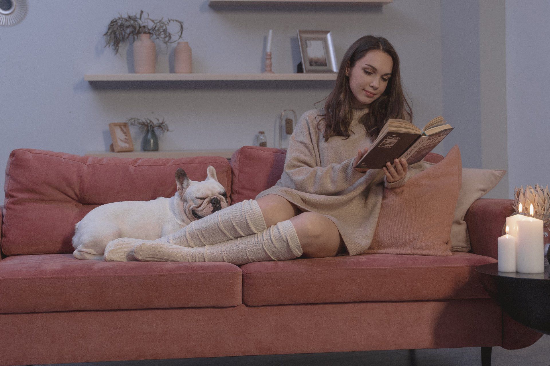 Woman relaxing on her sofa with her dog and reading a book. Candles are nearby to enhance the calm ambience.