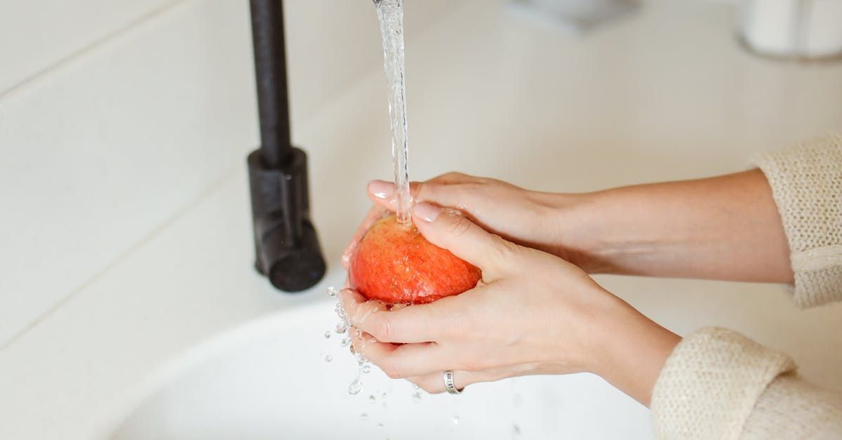 A woman is washing an apple in a sink  using filtered and softened water. 