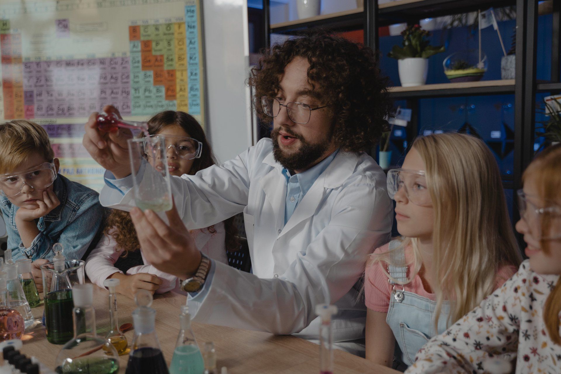 A man in a lab coat is teaching a group of children how to do a science experiment.