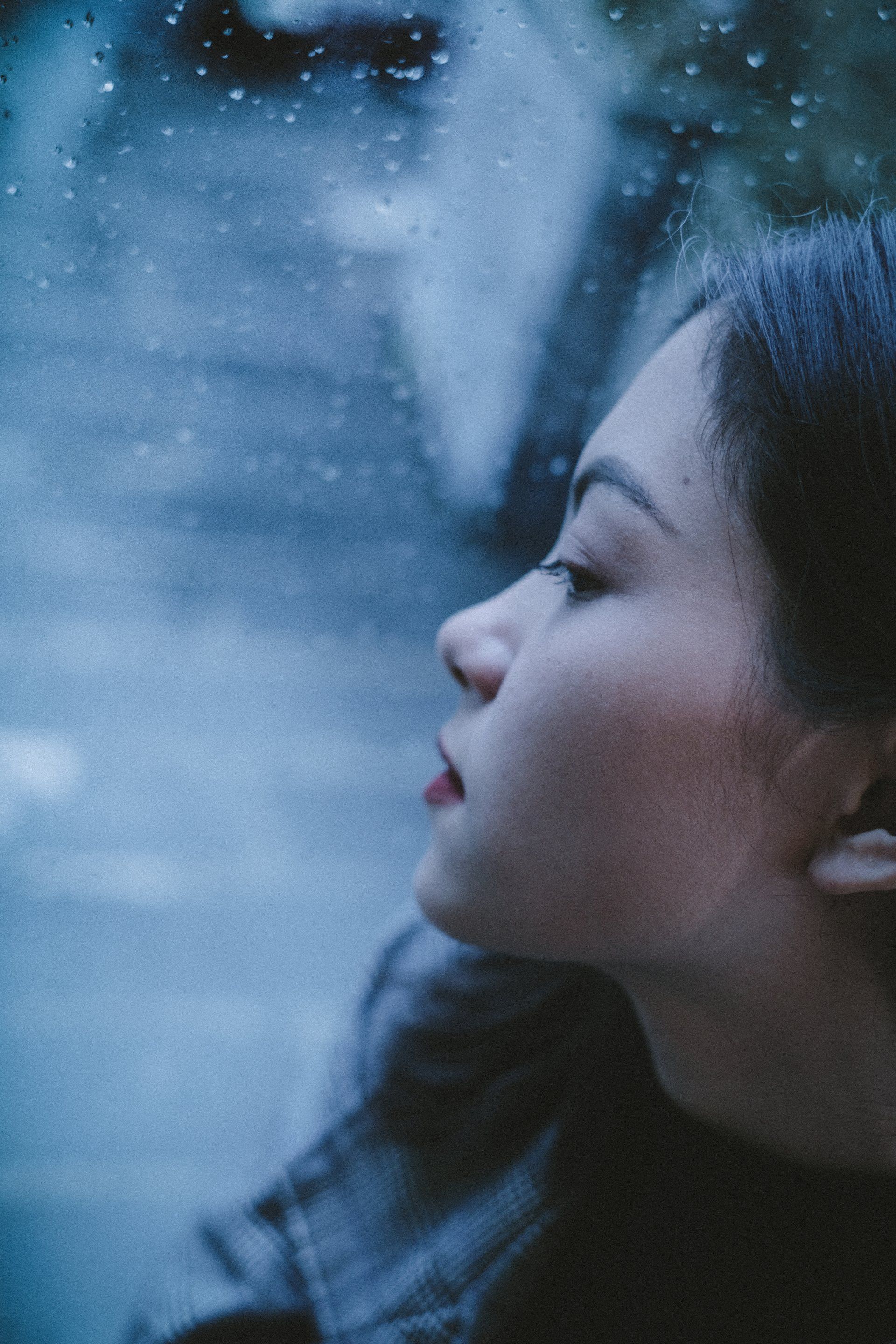 A woman is looking out of a window on a rainy day.