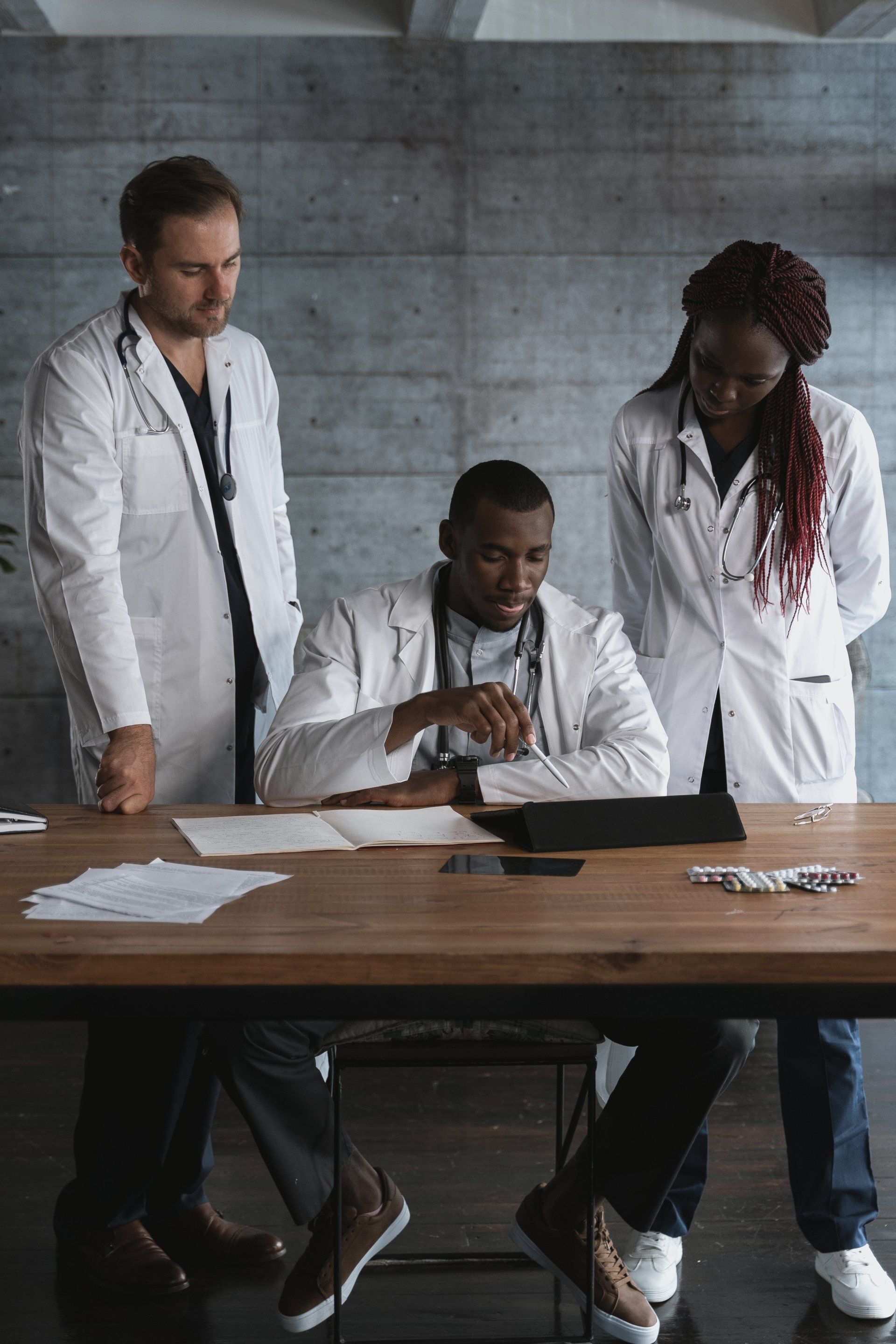 A group of doctors are sitting at a table looking at a tablet.