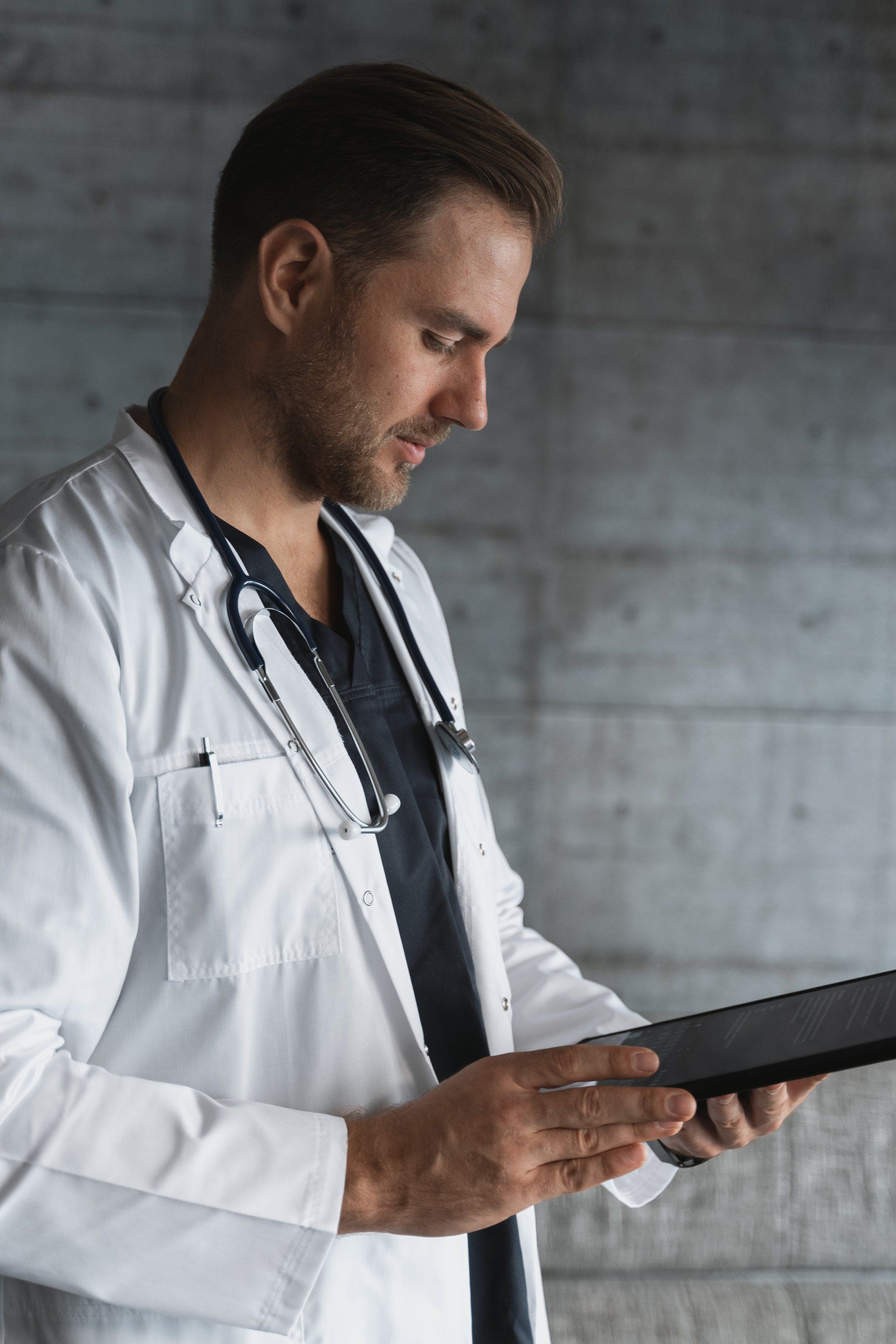 A doctor with a stethoscope around his neck is looking at a tablet computer.