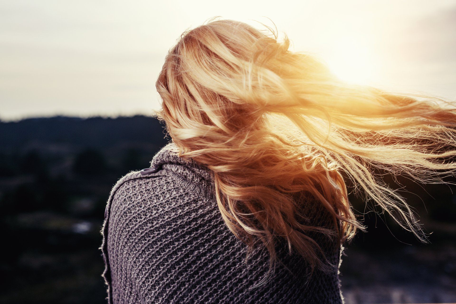 The woman is wearing a sweater and her hair is blowing in the wind.