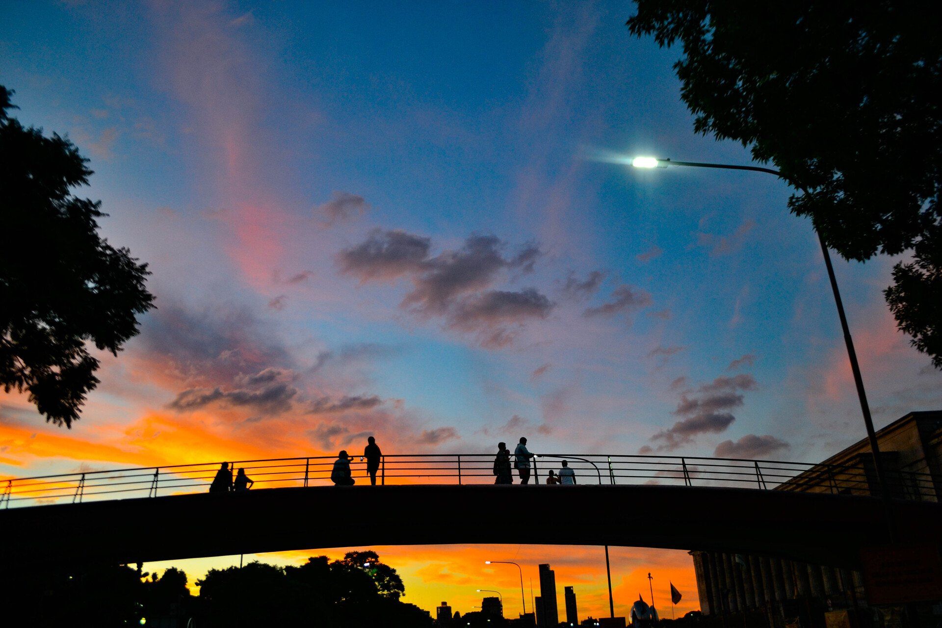 A group of people are walking across a bridge at sunset.